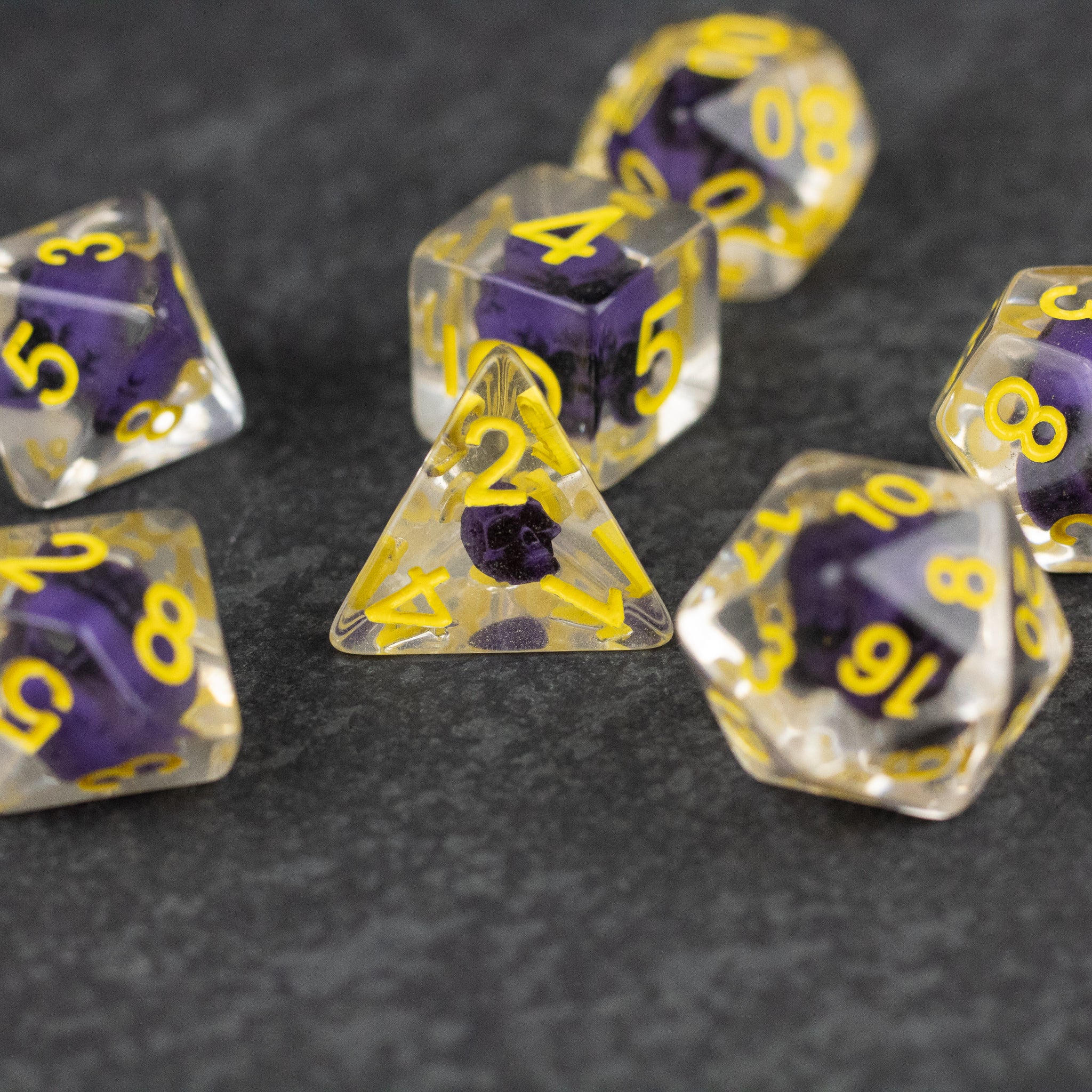 Purple Skull Dice Set - Purple and clear polyhedral dice set with yellow numbers and small skull designs inside each die.