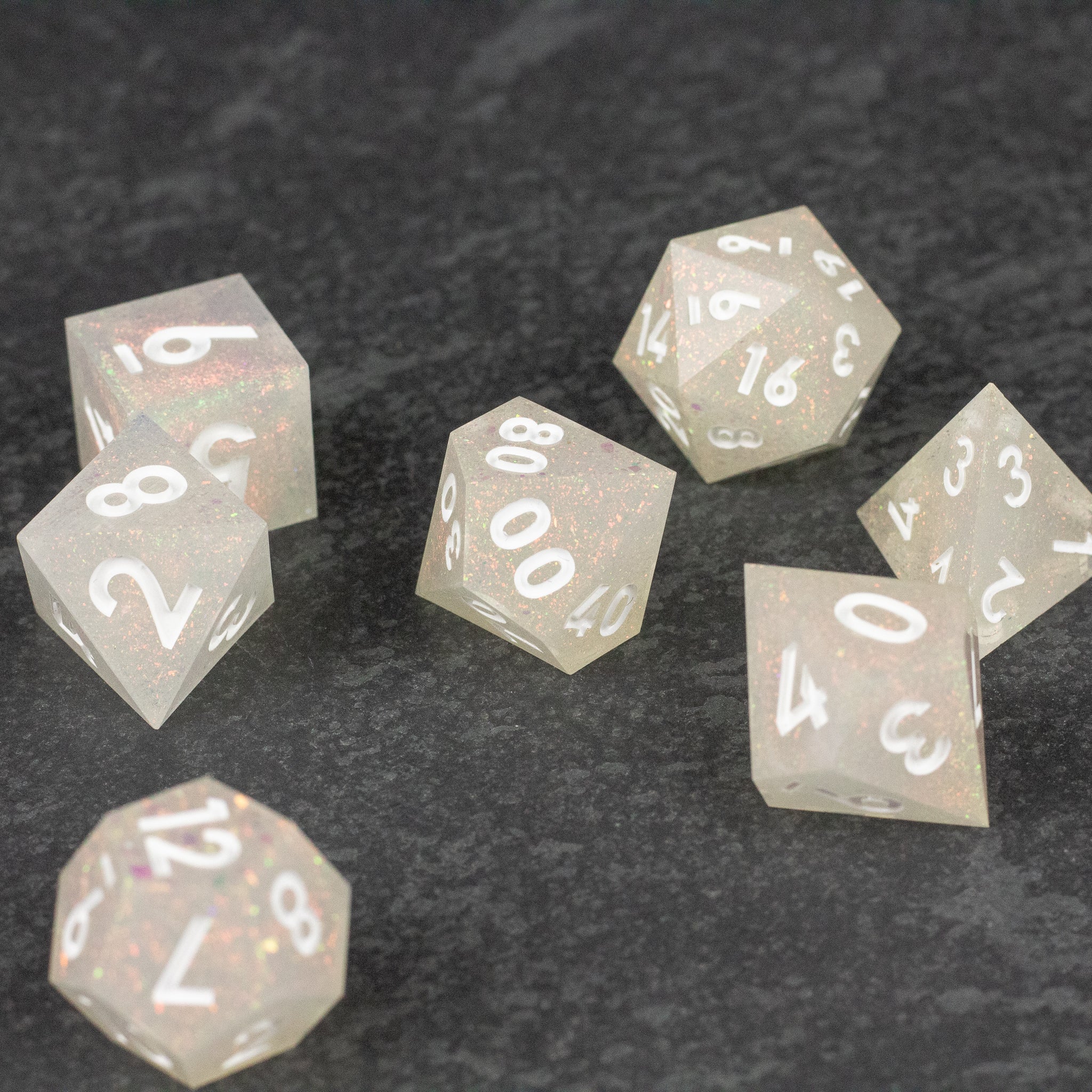 Snowfield Dice Set - Translucent white seven-piece polyhedral dice set with sharp edges and white numbering on a dark textured surface.