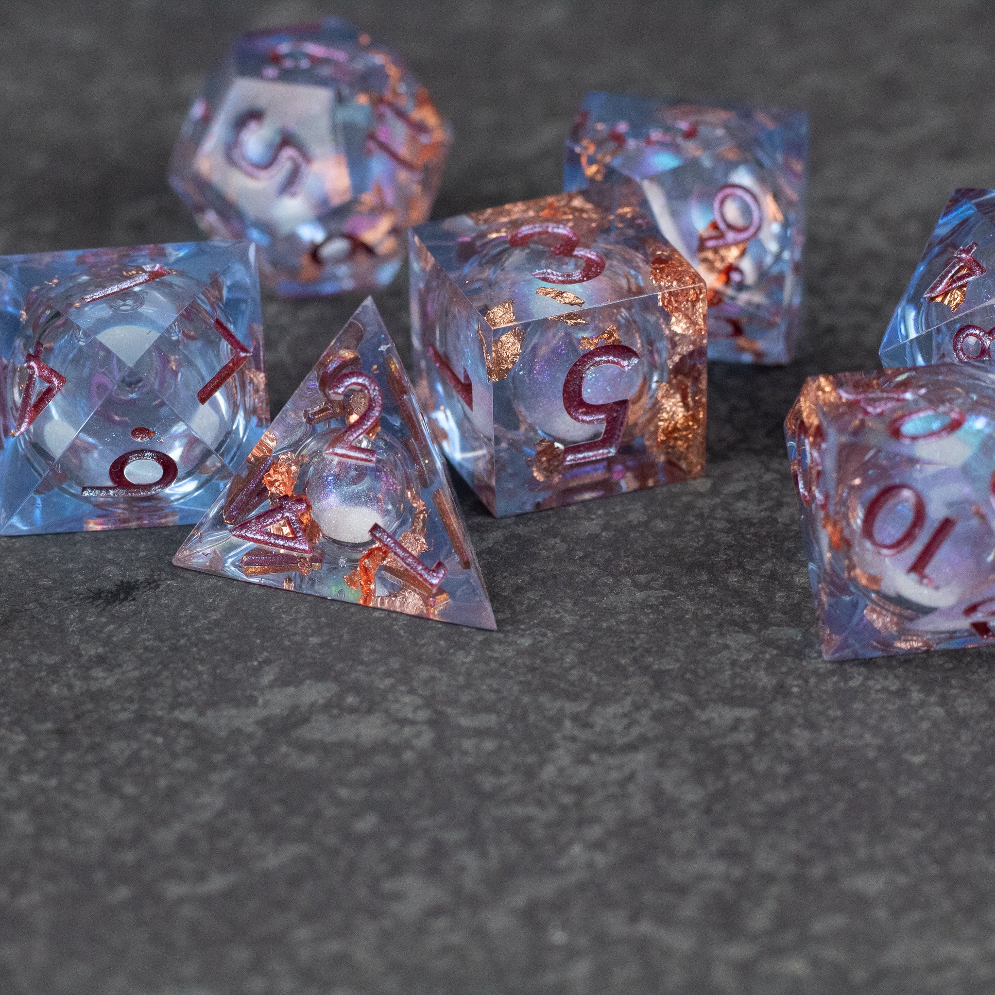 Temporal Rift Liquid Core Dice Set - Set of translucent blue polyhedral dice with sharp edges and swirling liquid core, featuring copper-colored numbers.
