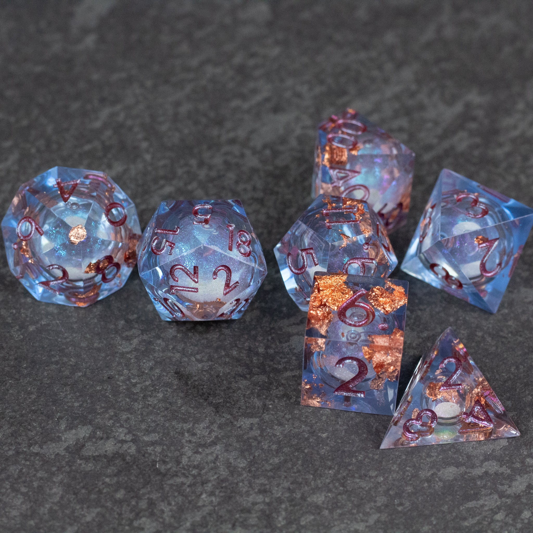 Temporal Rift Liquid Core Dice Set - Blue transparent sharp-edged polyhedral dice with swirling liquid core and metallic red numbers on dark surface.