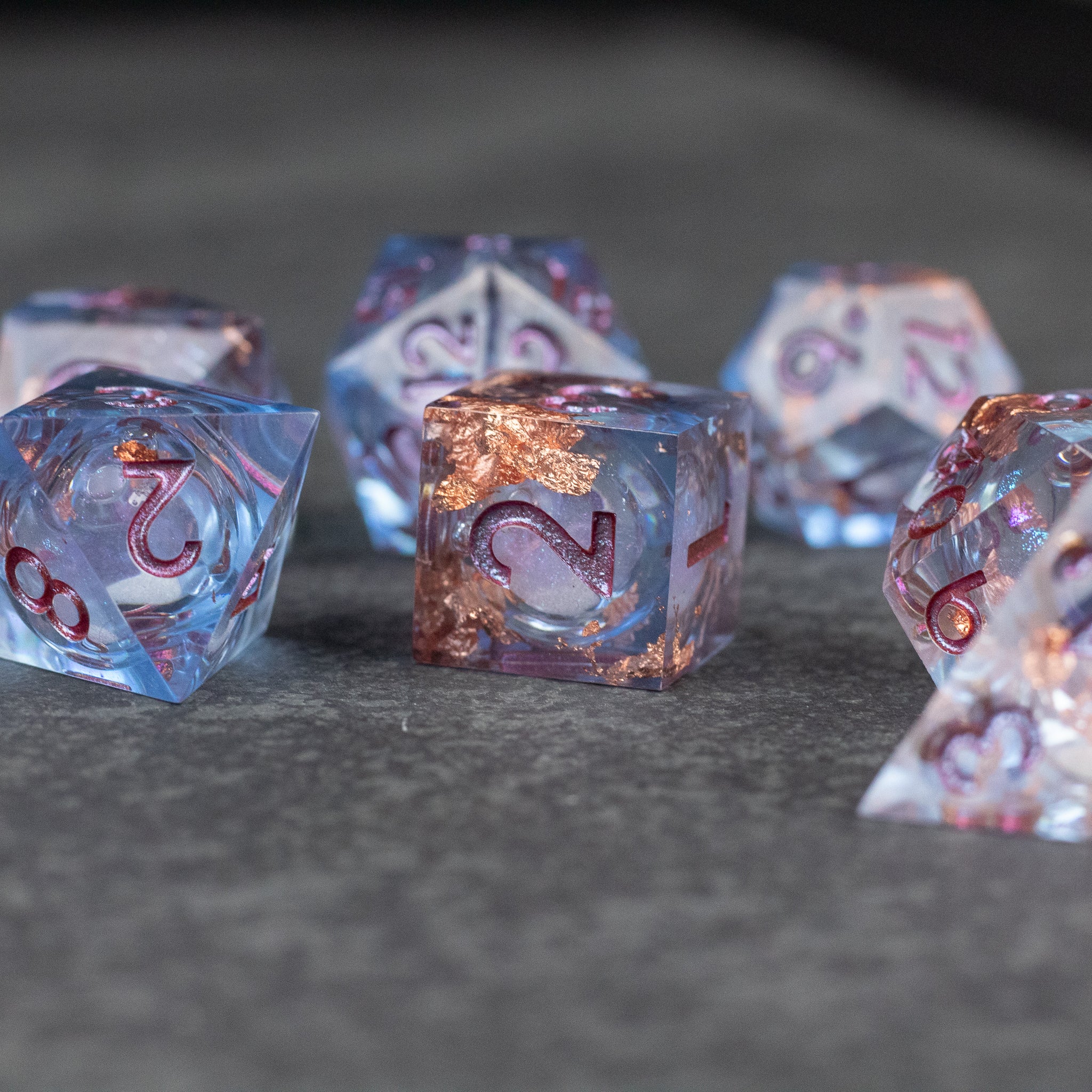 Temporal Rift Liquid Core Dice Set - Blue translucent sharp-edged dice set with liquid core and copper flakes inside on a dark surface.