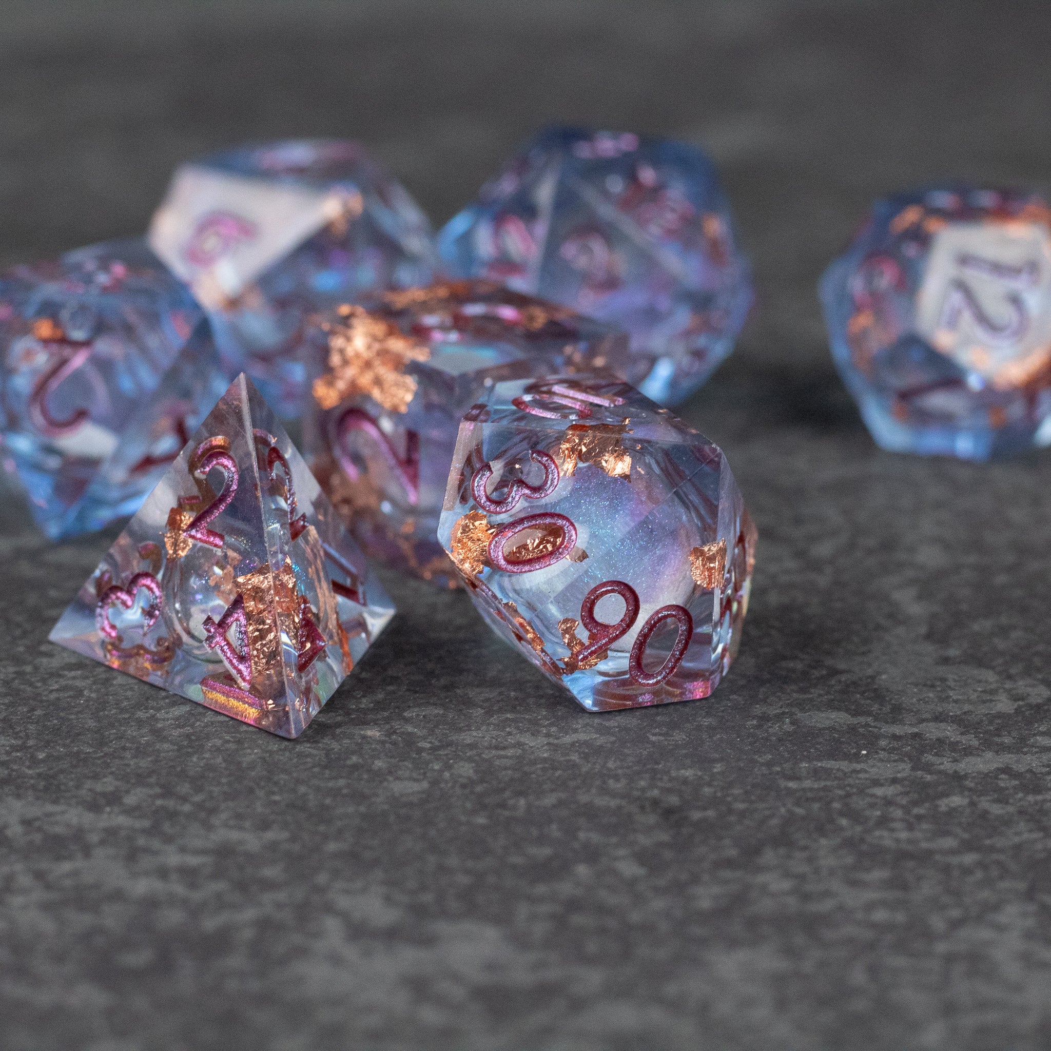 Temporal Rift Liquid Core Dice Set - Translucent blue seven-piece polyhedral dice set with gold numbering and sharp edges containing liquid core inclusions.