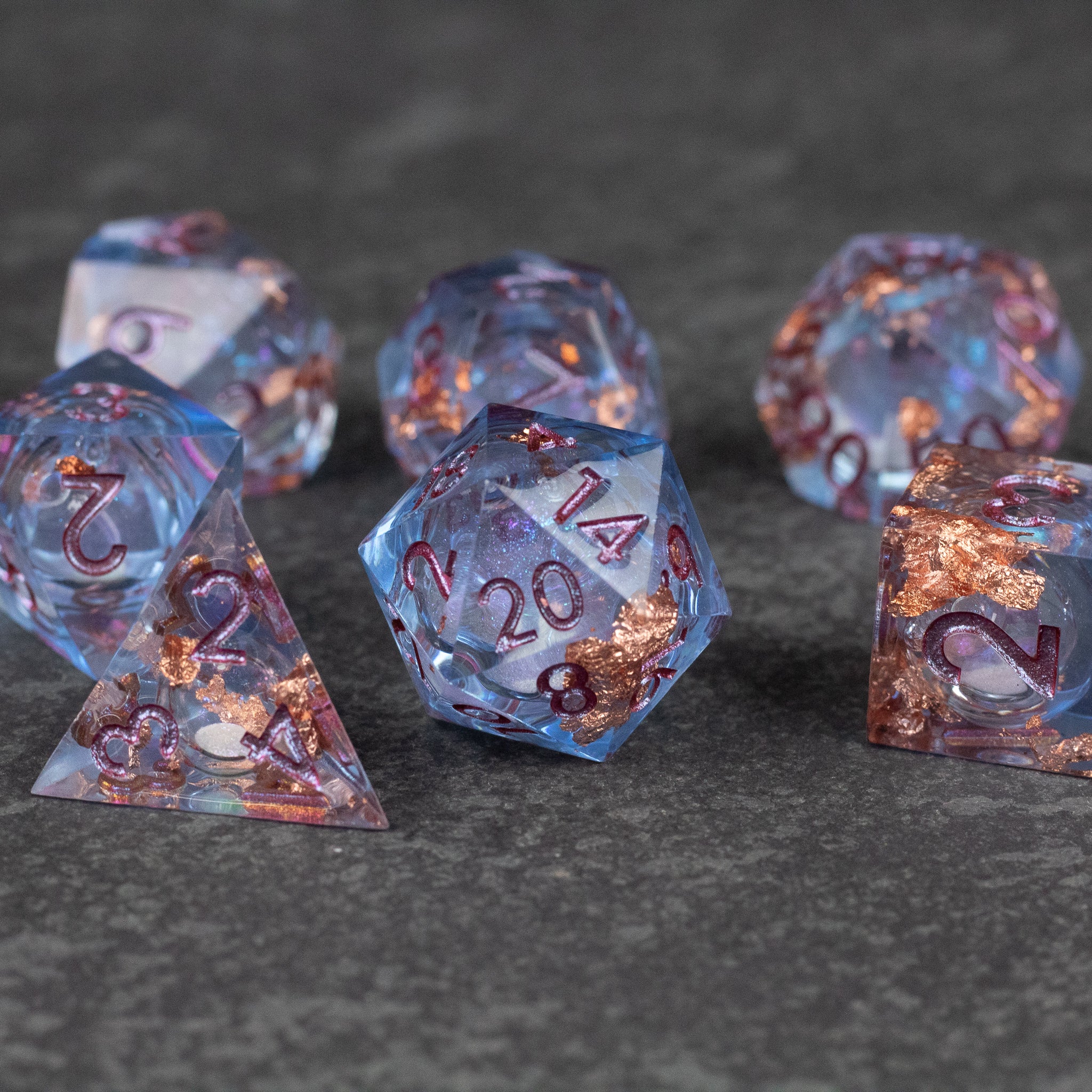 Temporal Rift Liquid Core Dice Set - Set of translucent blue sharp-edged dice with liquid core and copper-colored flecks inside, featuring red numbers.