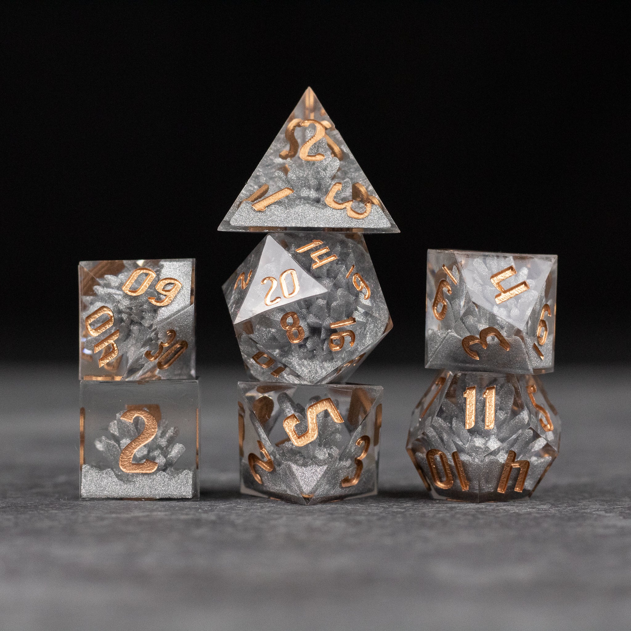 Silver Crystal Dice Set - Set of seven sharp-edged silver dice with copper-colored numbers on a smoky background.
