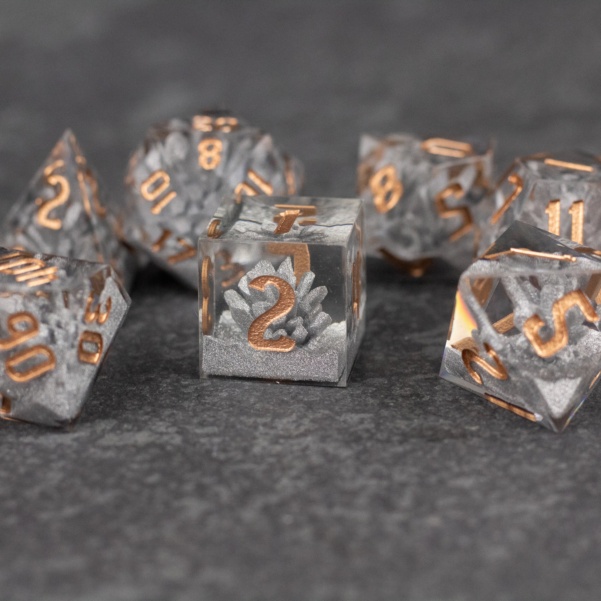Silver Crystal Dice Set - Silver transparent dice set with sharp edges and gold metallic numbers on a dark gray surface.