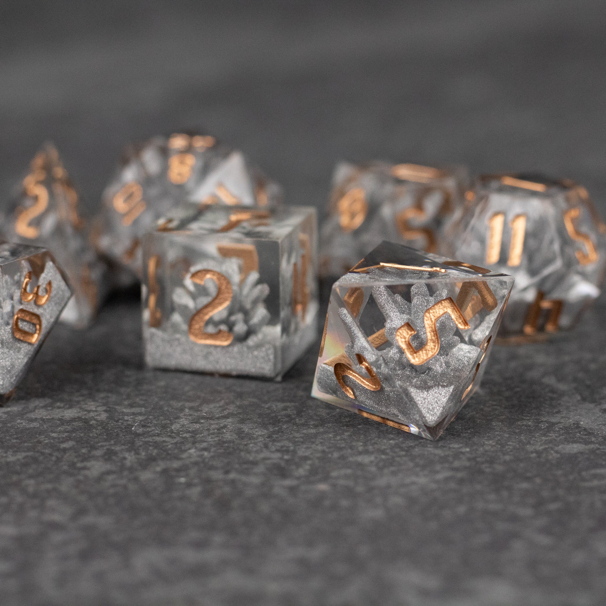 Silver Crystal Dice Set - Set of silver polyhedral dice with sharp edges and copper-colored numbers on gray surface.