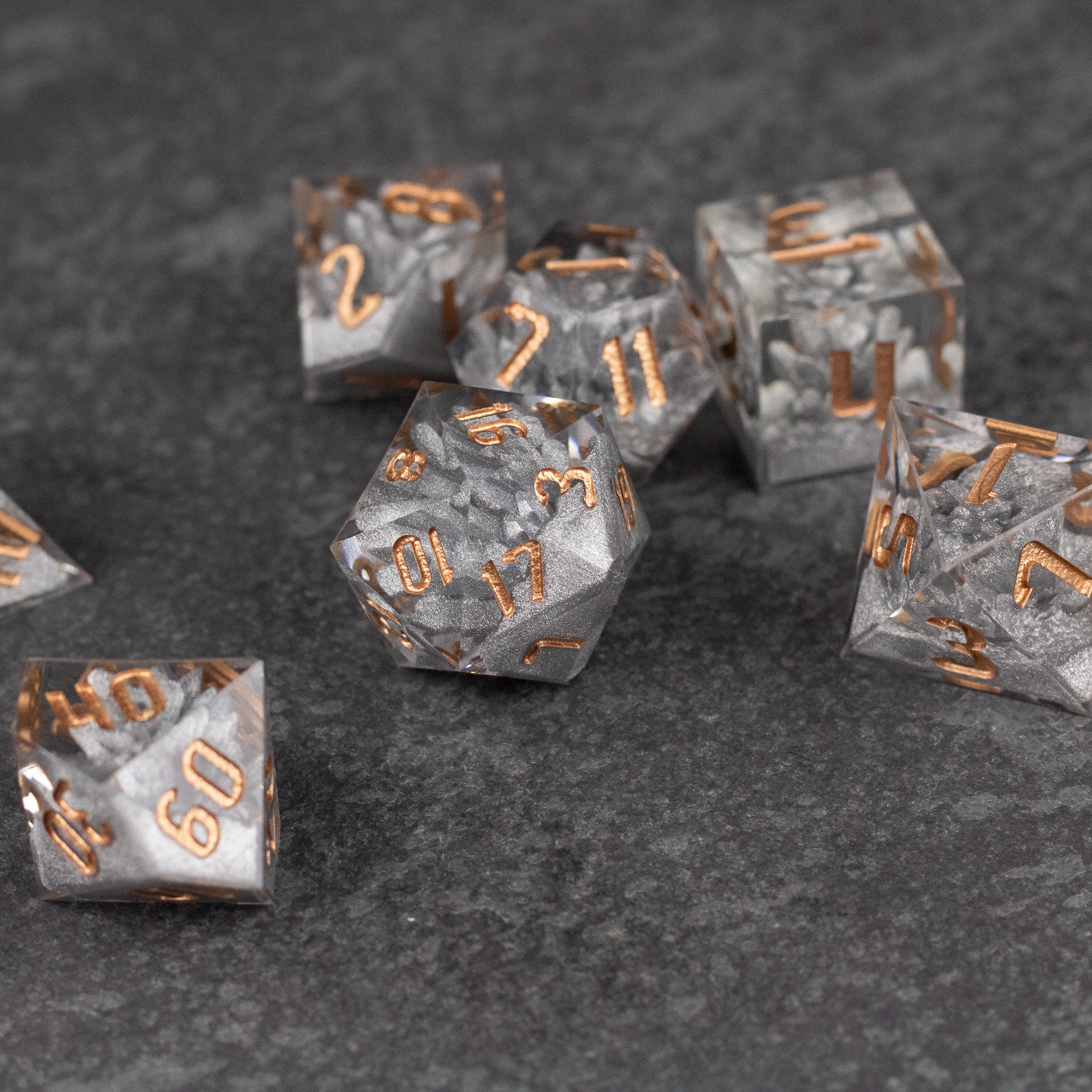 Silver Crystal Dice Set - Set of transparent silver crystal polyhedral dice with sharp edges and copper-colored numbers on dark textured background.