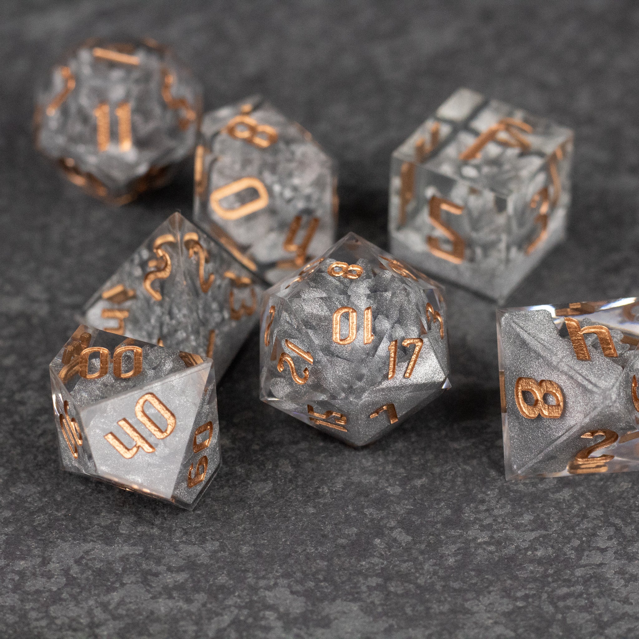 Silver Crystal Dice Set - Set of seven silver translucent sharp-edged dice with metallic gold numbers on dark gray textured background.