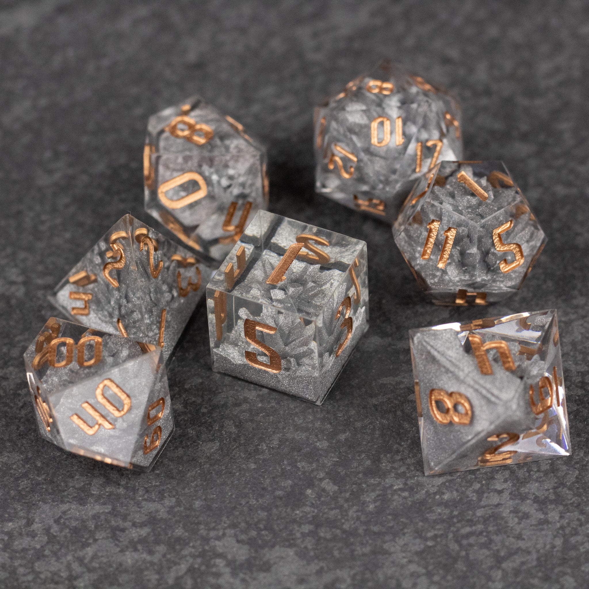 Silver Crystal Dice Set - Set of seven silver crystal dice with sharp edges and gold engraved numbers on a dark gray textured surface.