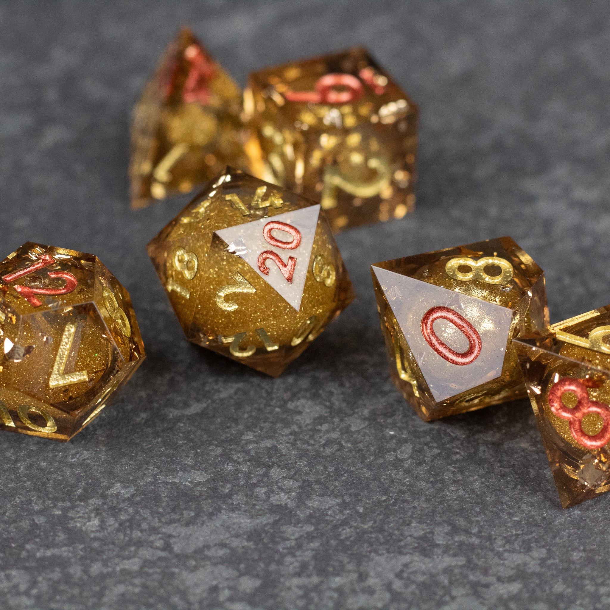 Dragon's Hoard Liquid Core Dice Set - Gold liquid core polyhedral dice set with sharp edges and red numbering on gray surface.
