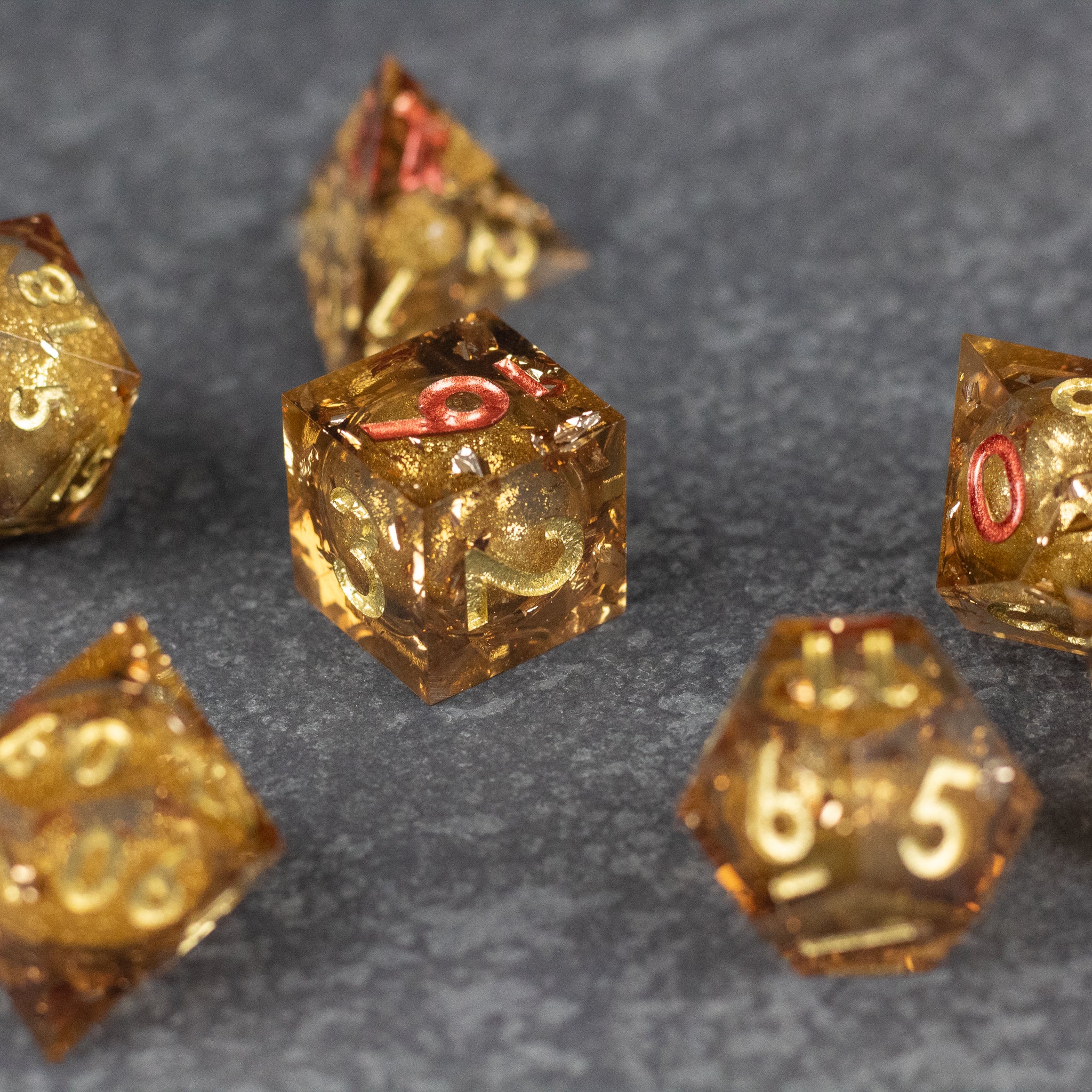 Dragon's Hoard Liquid Core Dice Set - Gold sharp-edged dice set with liquid core and red numbering on dark textured surface.