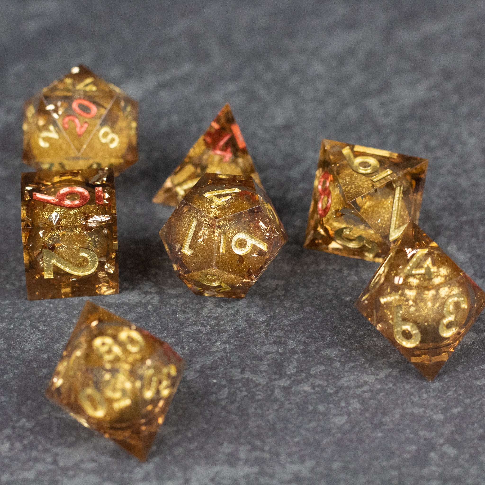 Dragon's Hoard Liquid Core Dice Set - Set of seven translucent gold polyhedral dice with sharp edges and red numbers, containing swirling liquid cores.