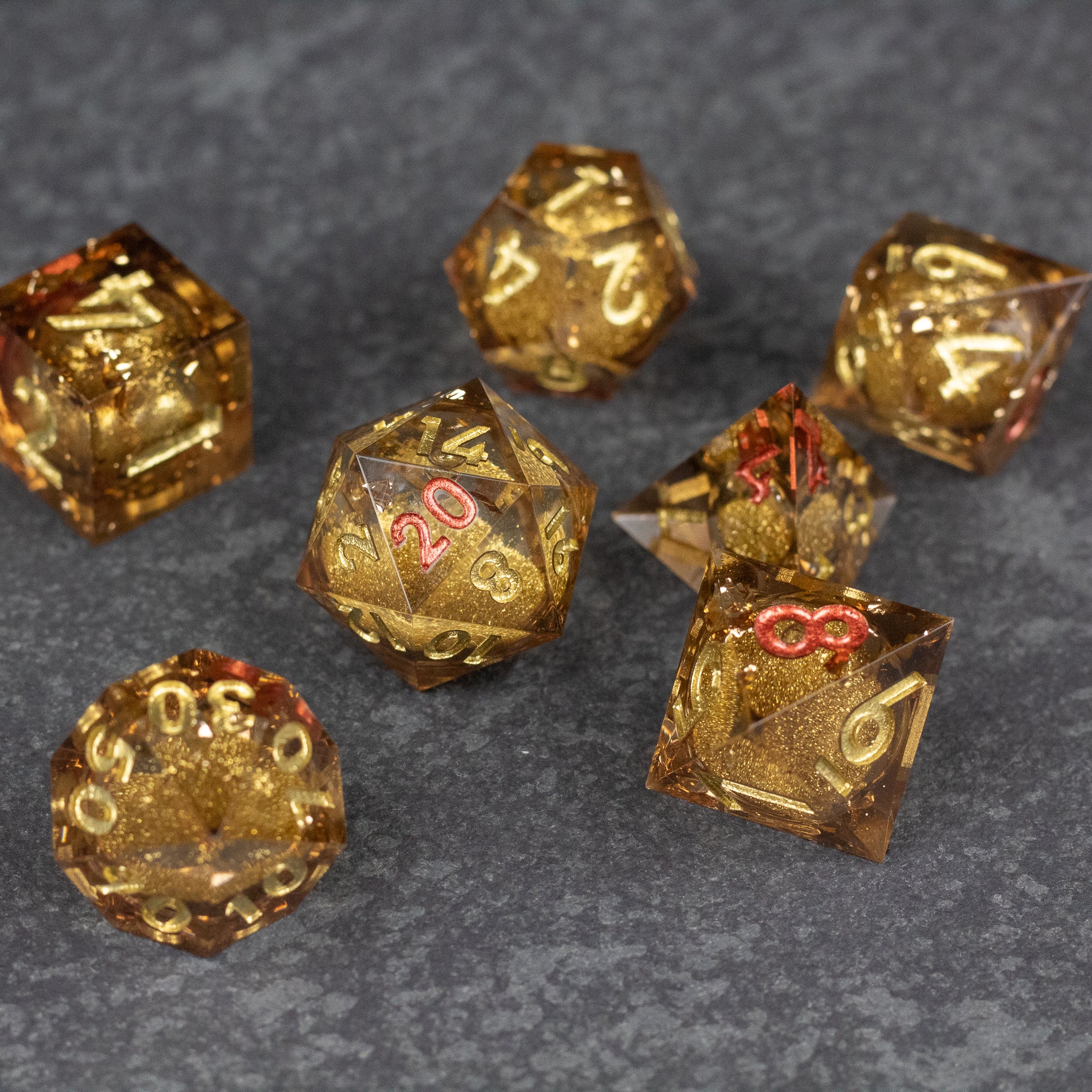 Dragon's Hoard Liquid Core Dice Set - Seven gold, translucent sharp-edged polyhedral dice with liquid core and dragon scale inclusions, including d20, d12, d10,.