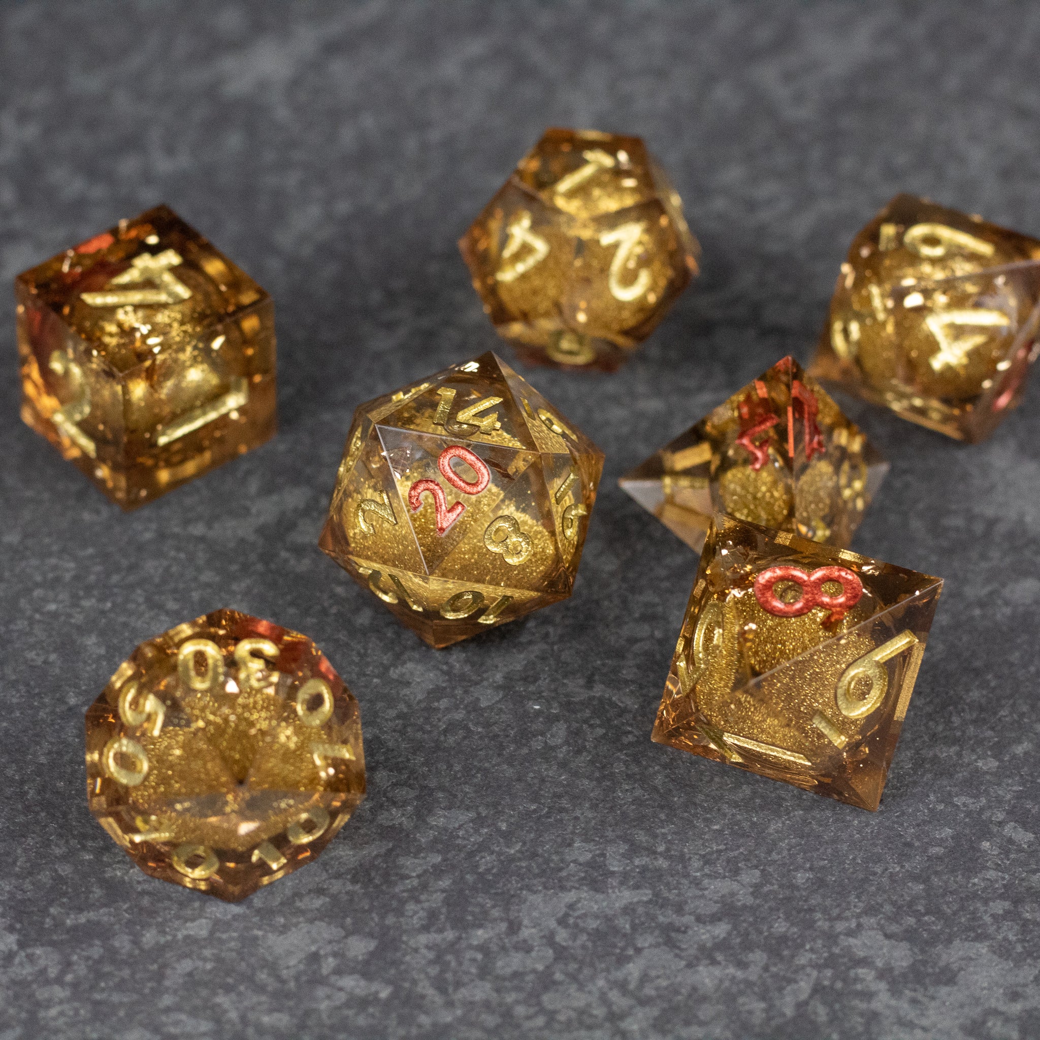 Dragon's Hoard Liquid Core Dice Set - Gold sharp-edged polyhedral dice with liquid core and metallic gold numbering on dark gray surface.