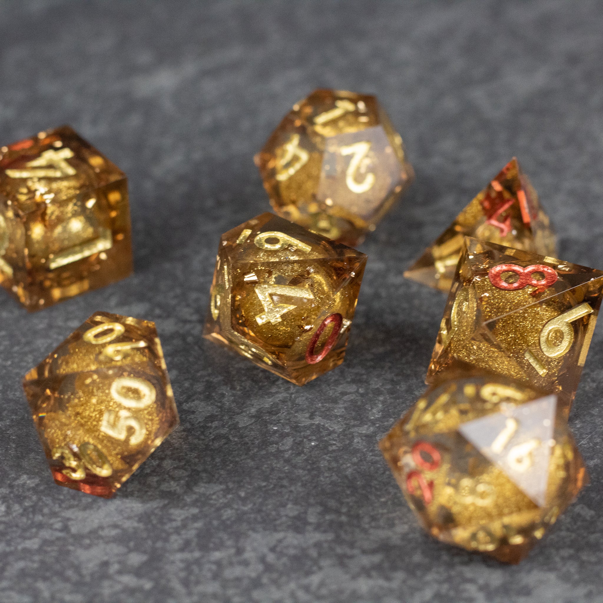 Dragon's Hoard Liquid Core Dice Set - Set of sharp-edged gold polyhedral dice with transparent liquid core and white and red numbering.