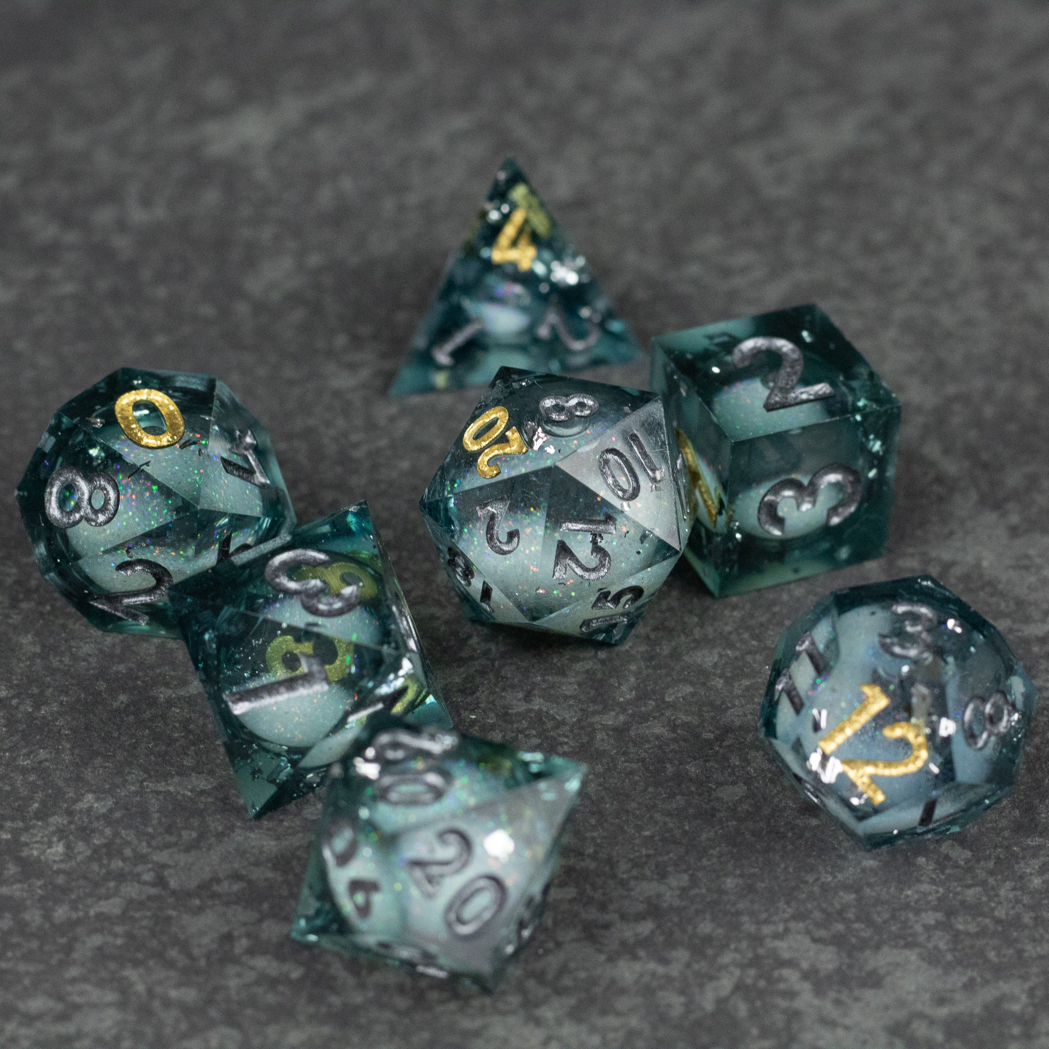 Call Of The Deep - Liquid Core Dice Set - Translucent dark blue liquid-core seven-piece polyhedral dice set with gold and silver numbering and sharp edges.