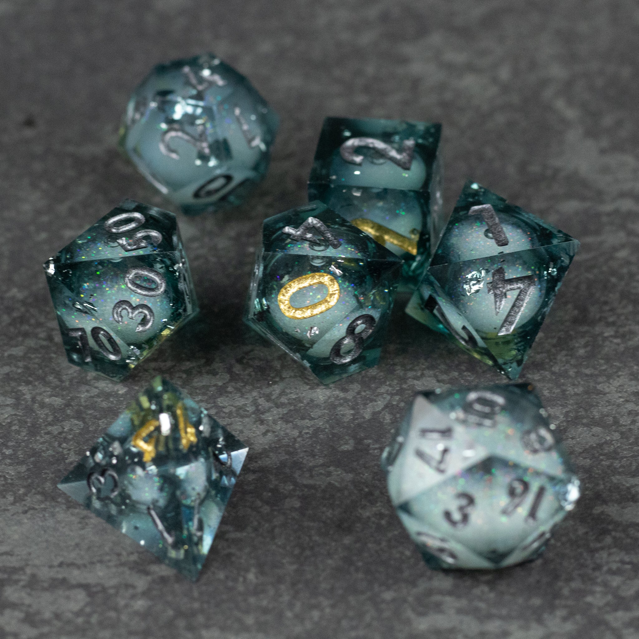 Call Of The Deep - Liquid Core Dice Set - Set of six translucent, deep green liquid core dice with gold and black speckles and sharp edges on gray surface.