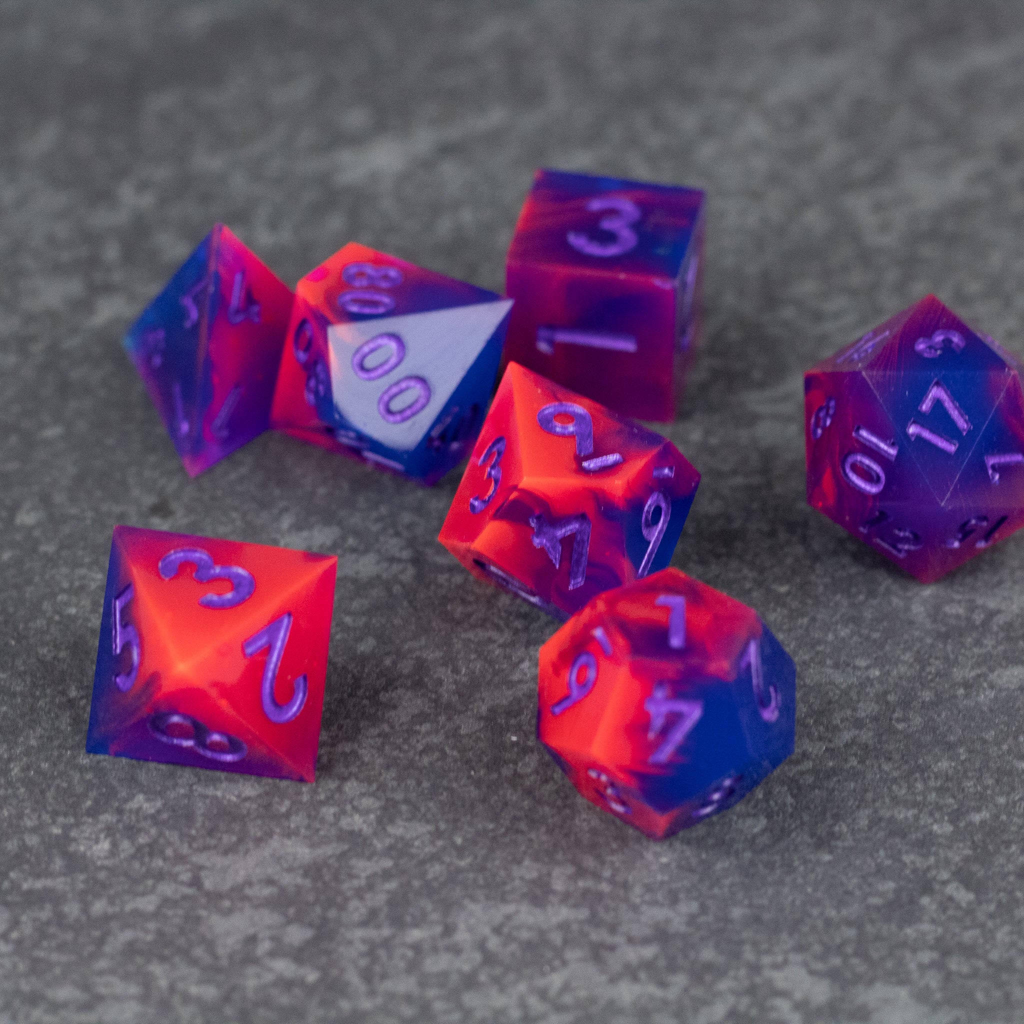 Outrun Dice Set - Sharp-edged polyhedral dice set in vibrant orange and purple neon swirl with white numbering on gray surface.