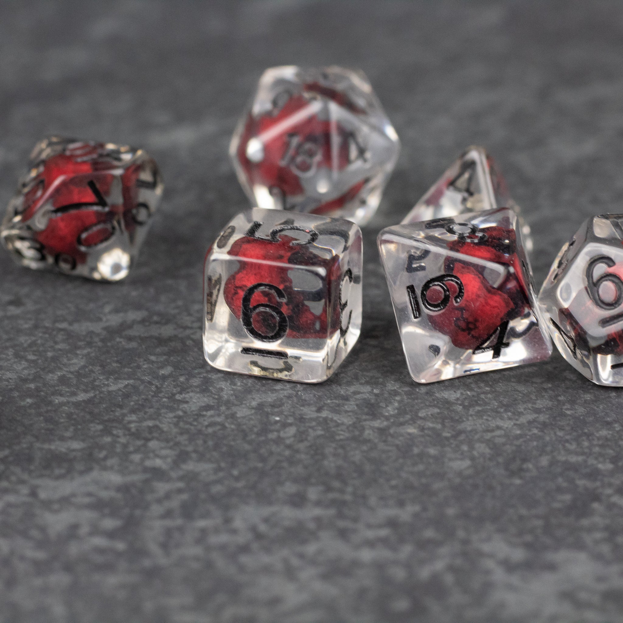 Red Skull Dice Set - Transparent polyhedral dice set with red skull inclusions and black numbers on a dark surface.