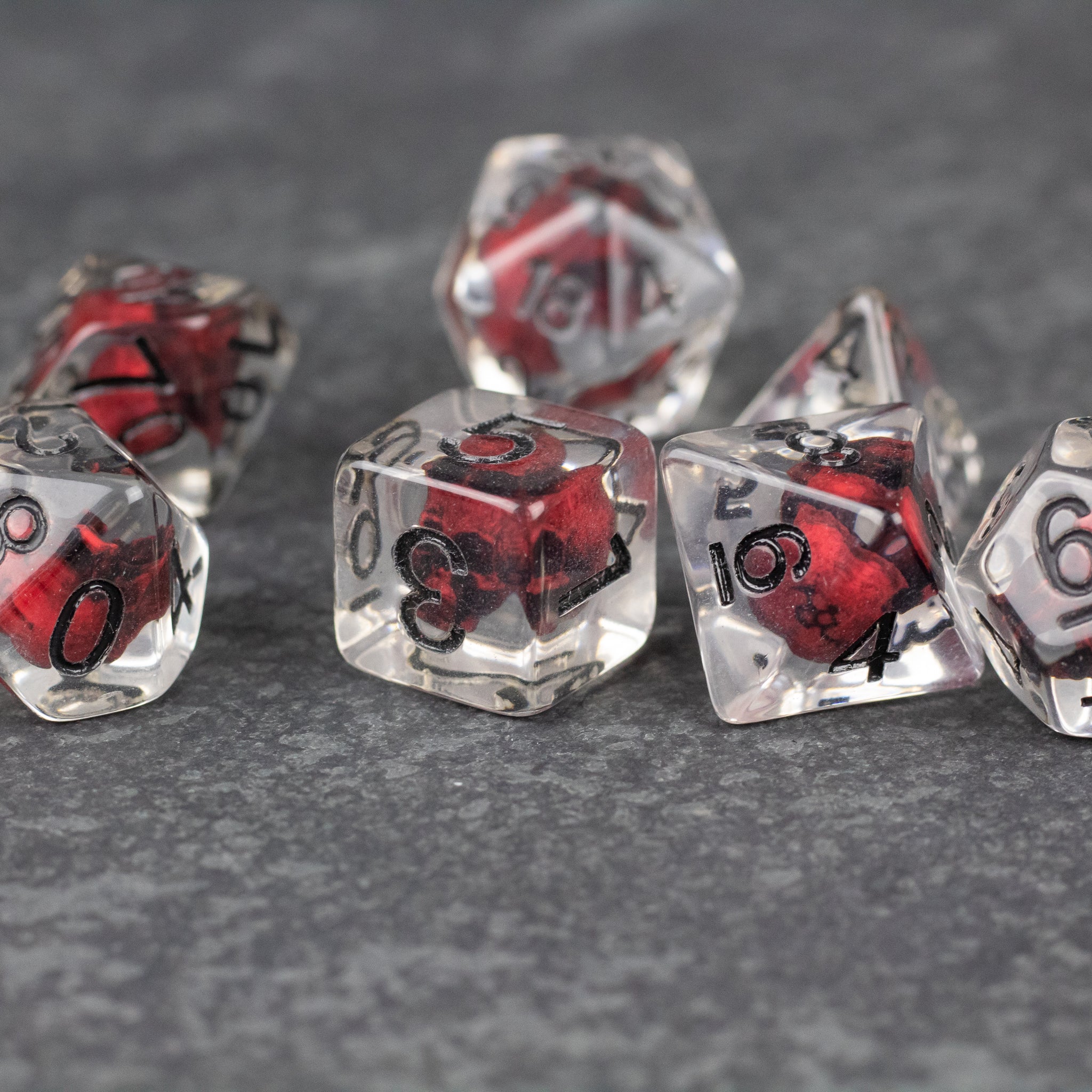 Red Skull Dice Set - Clear poly dice with red skull inclusions and black numbering, set on gray surface.
