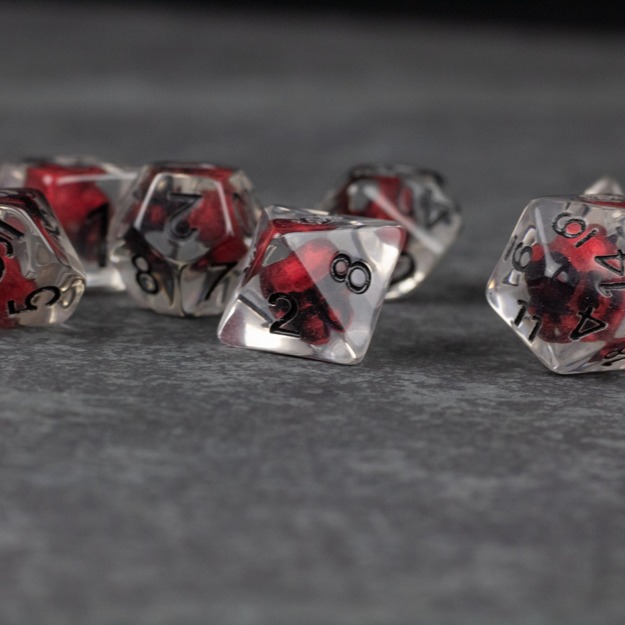 Red Skull Dice Set - Transparent dice with red skull designs inside and black numbering, set on a gray surface.