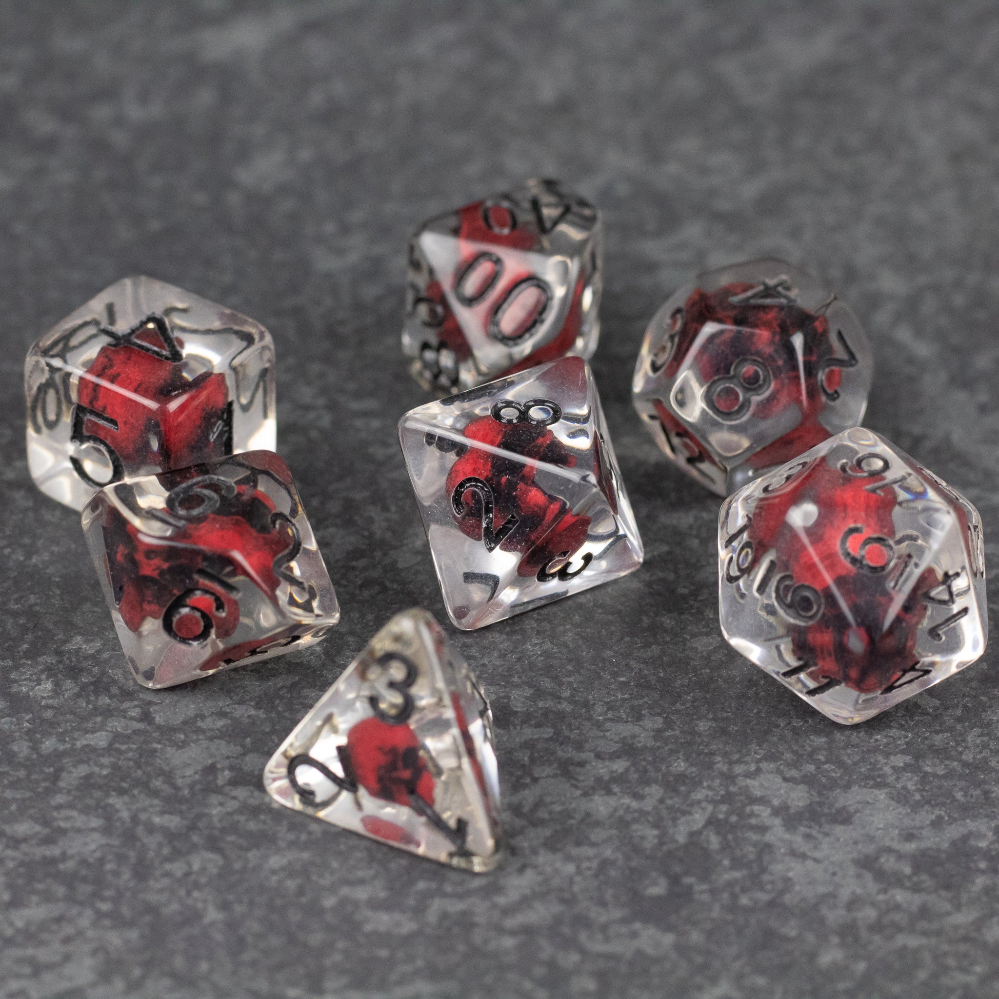 Red Skull Dice Set - Set of seven clear polyhedral dice with suspended red skulls inside and black numbering on each face.