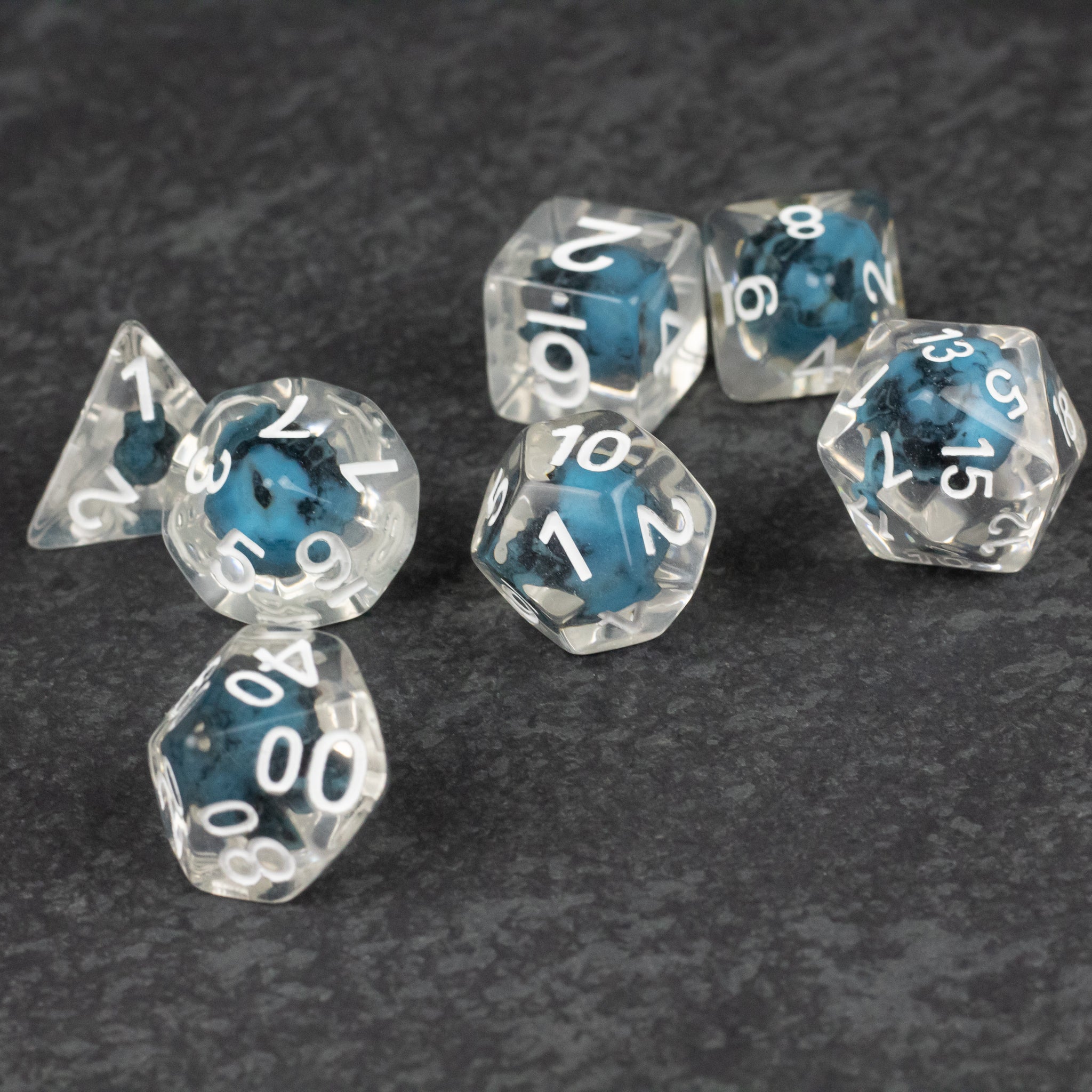 Blue Skull Dice Set - Set of seven clear polyhedral dice with blue smoky cores and white numbers, including a d20, d12, d10, and d8.