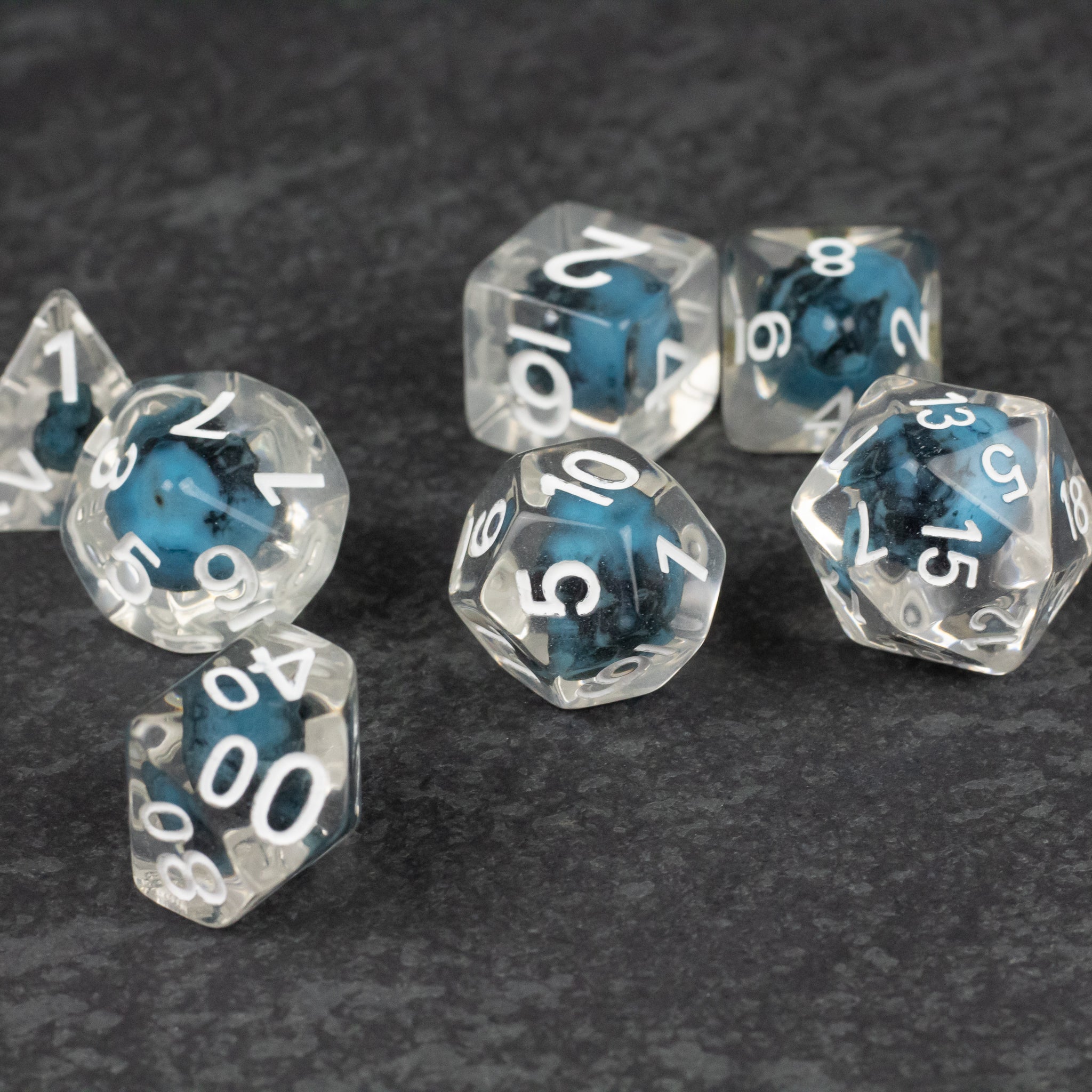 Blue Skull Dice Set - Clear polyhedral dice set with embedded blue skulls and white numbers on a dark gray surface.