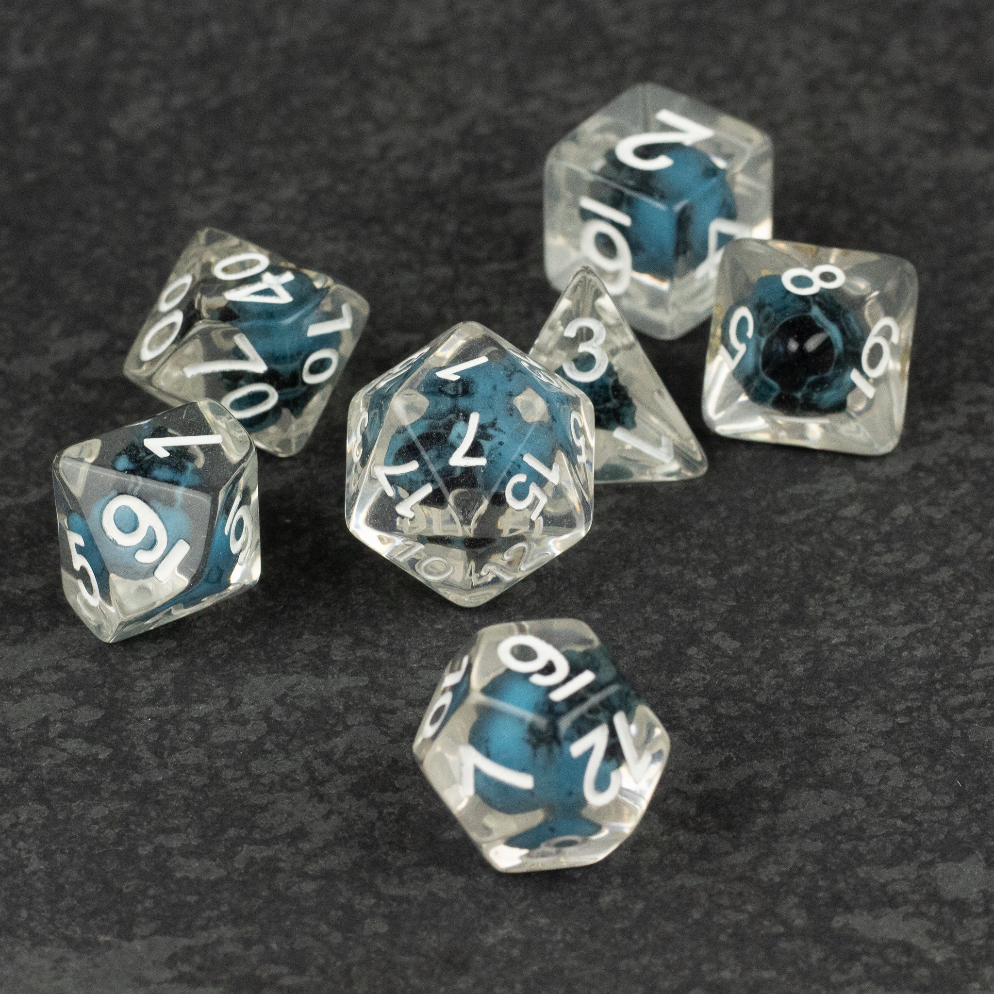 Blue Skull Dice Set - Set of seven translucent blue and clear polyhedral dice with white numbers and skull designs inside, including d4, d6, d8,.