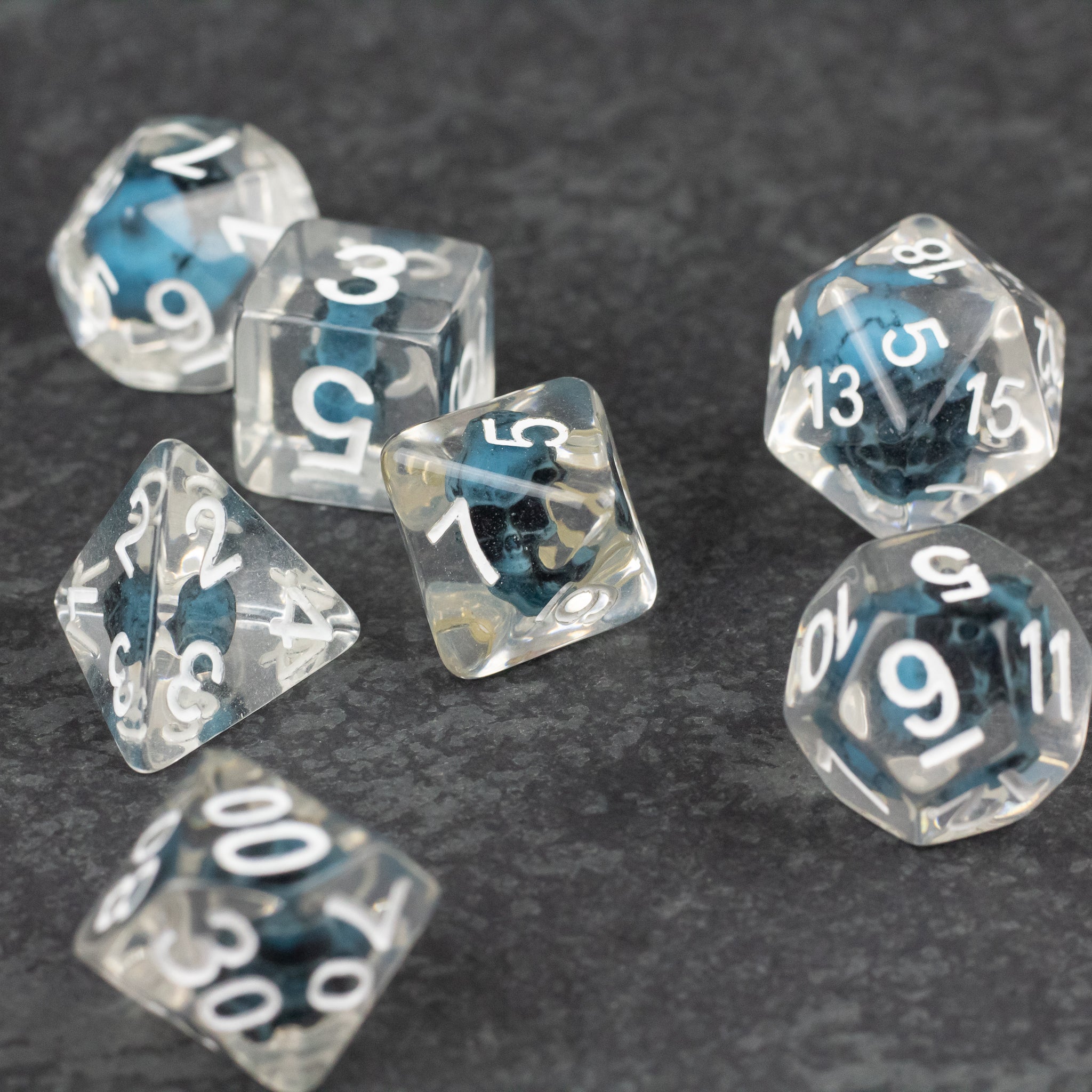 Blue Skull Dice Set - Seven transparent polyhedral dice with blue skulls inside and white numbering.