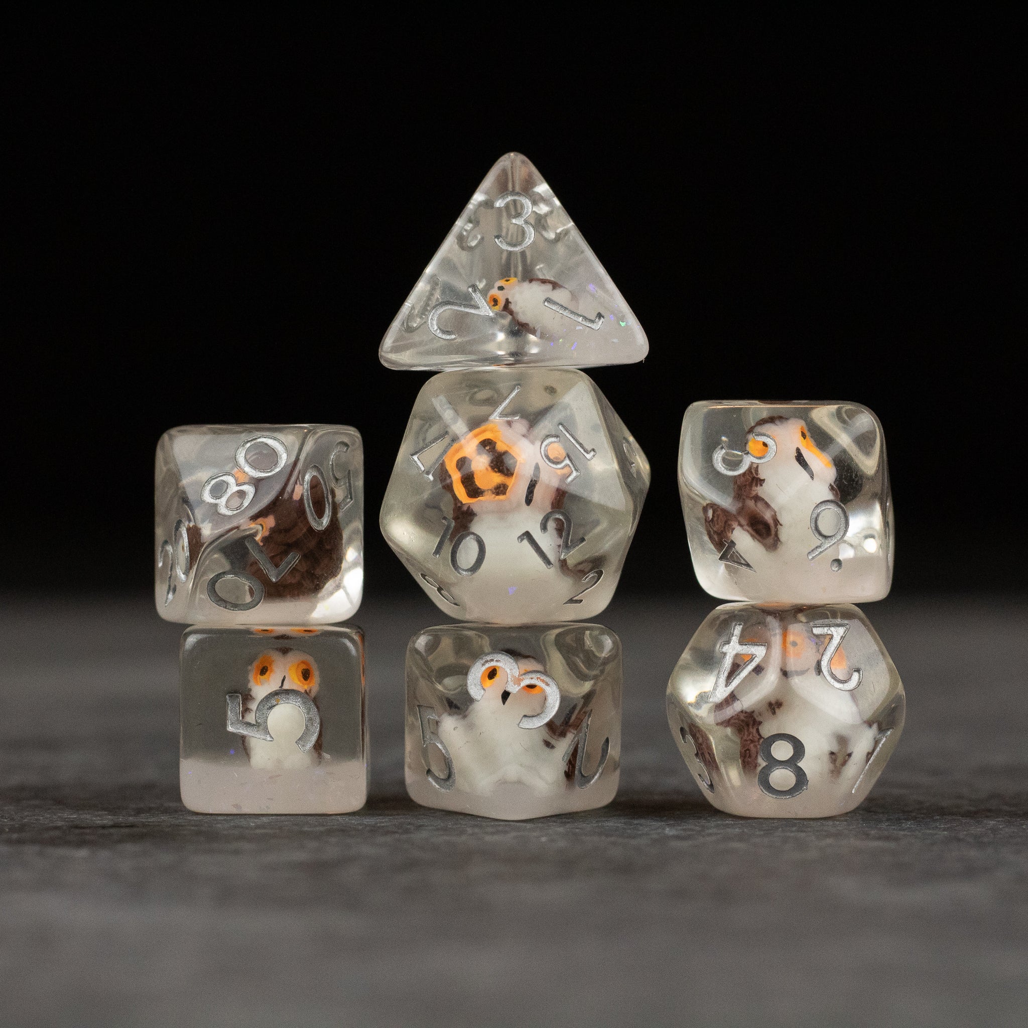 Owl Dice Set - Seven transparent polyhedral dice with small detailed owl figures inside, featuring white and orange numbering on each die.