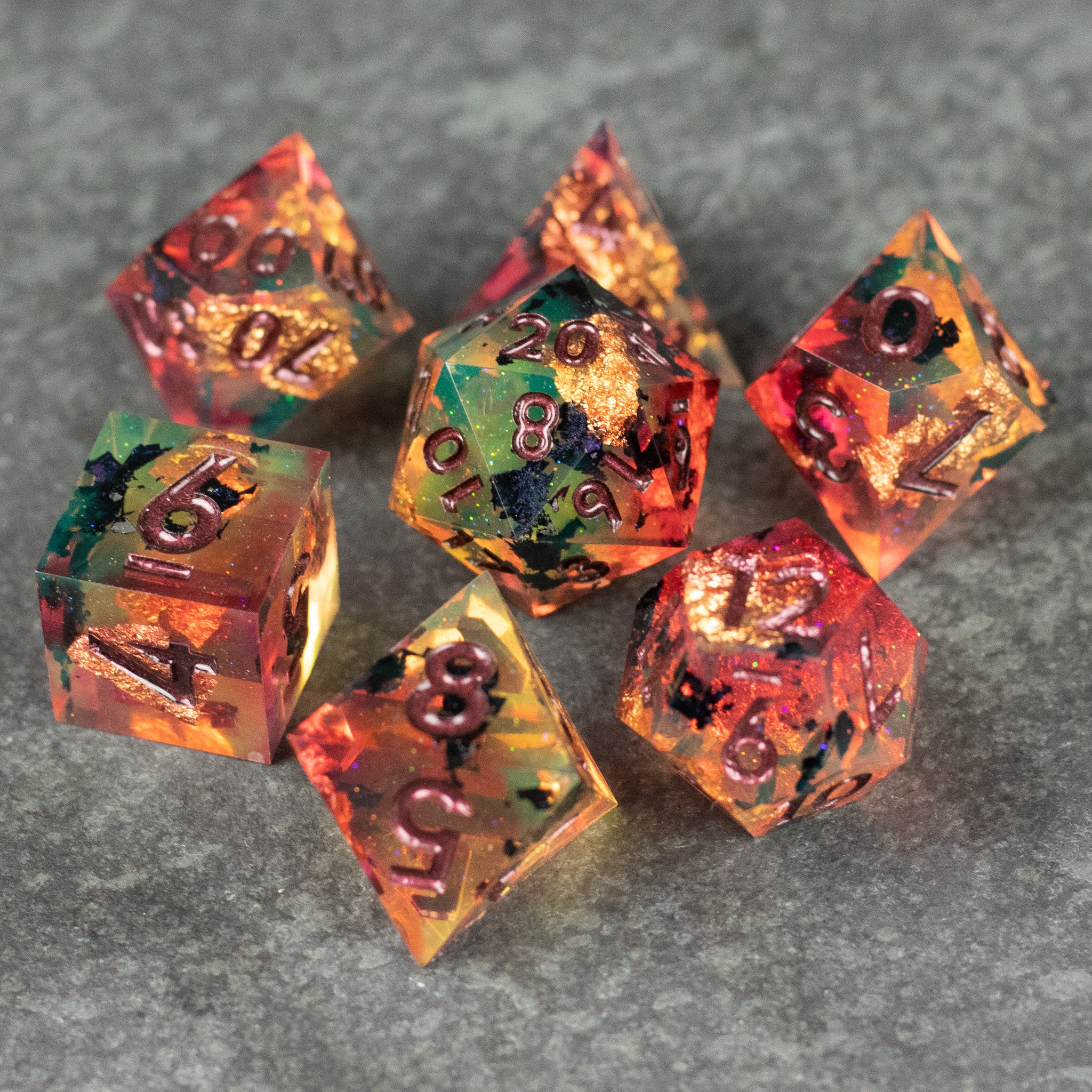 Dawn Ritual Dice Set - Sharp edge polyhedral dice set with red, orange, and green swirls and black numbers on gray surface.