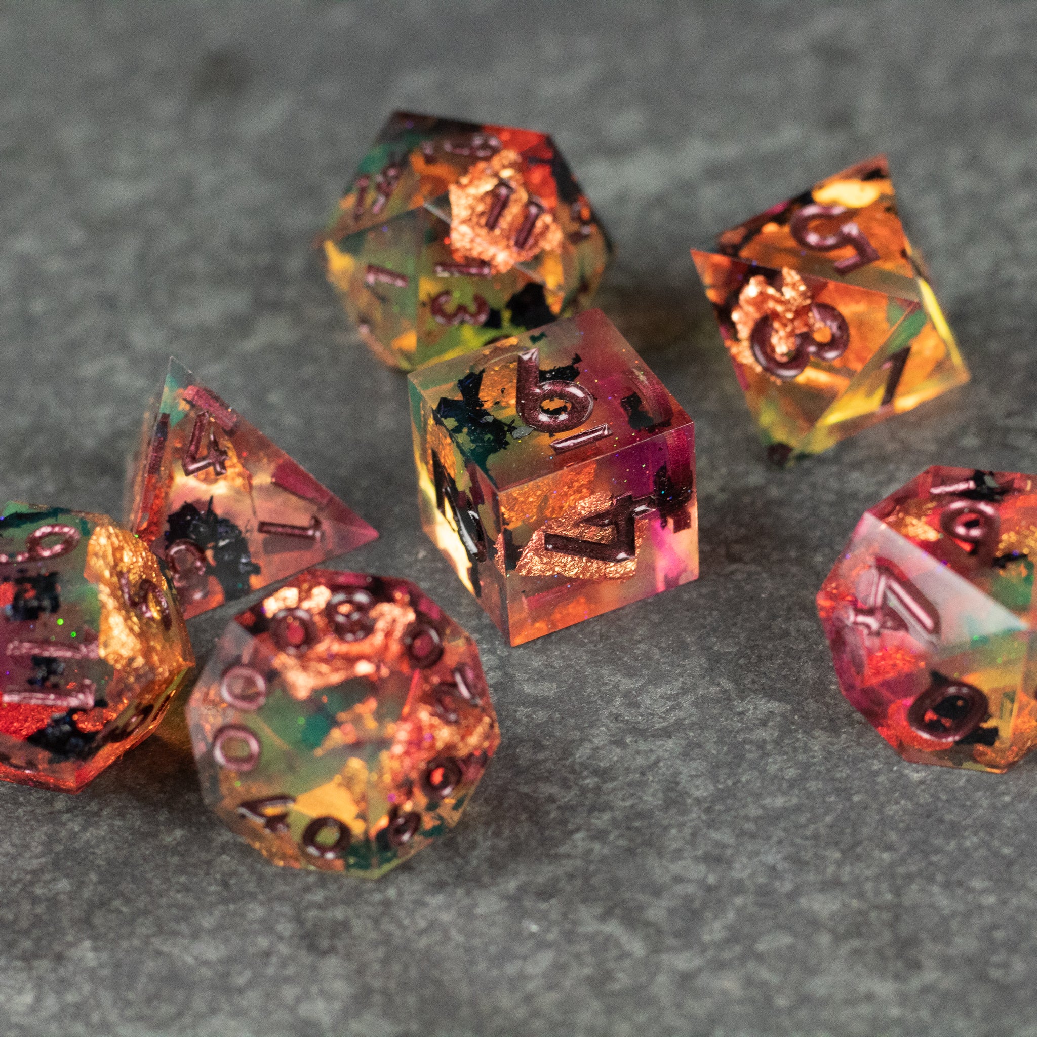 Dawn Ritual Dice Set - Set of seven translucent polyhedral dice with embedded fiery orange and gold flakes and sharp edges on gray surface.