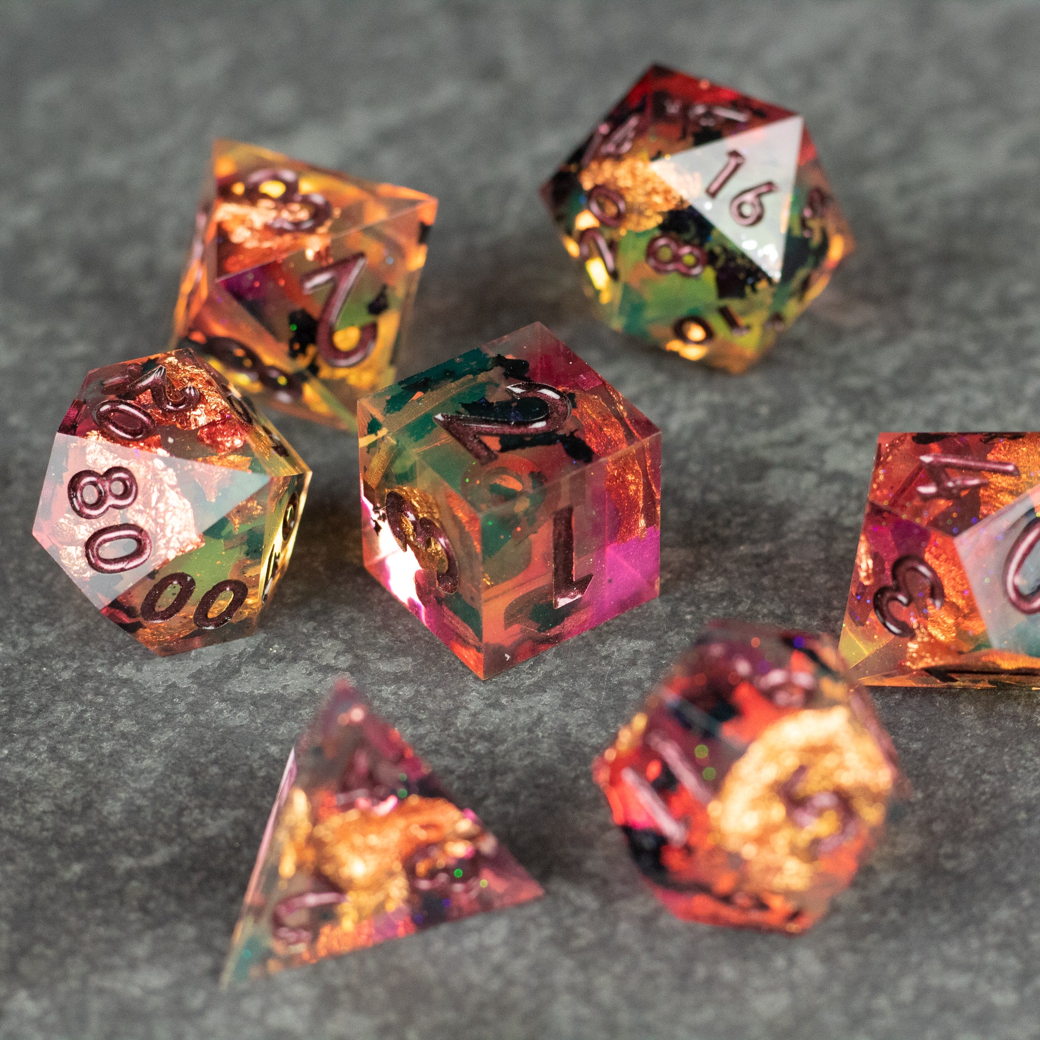 Dawn Ritual Dice Set - Multicolored sharp edge polyhedral dice set with pink, gold, and green hues on gray surface.