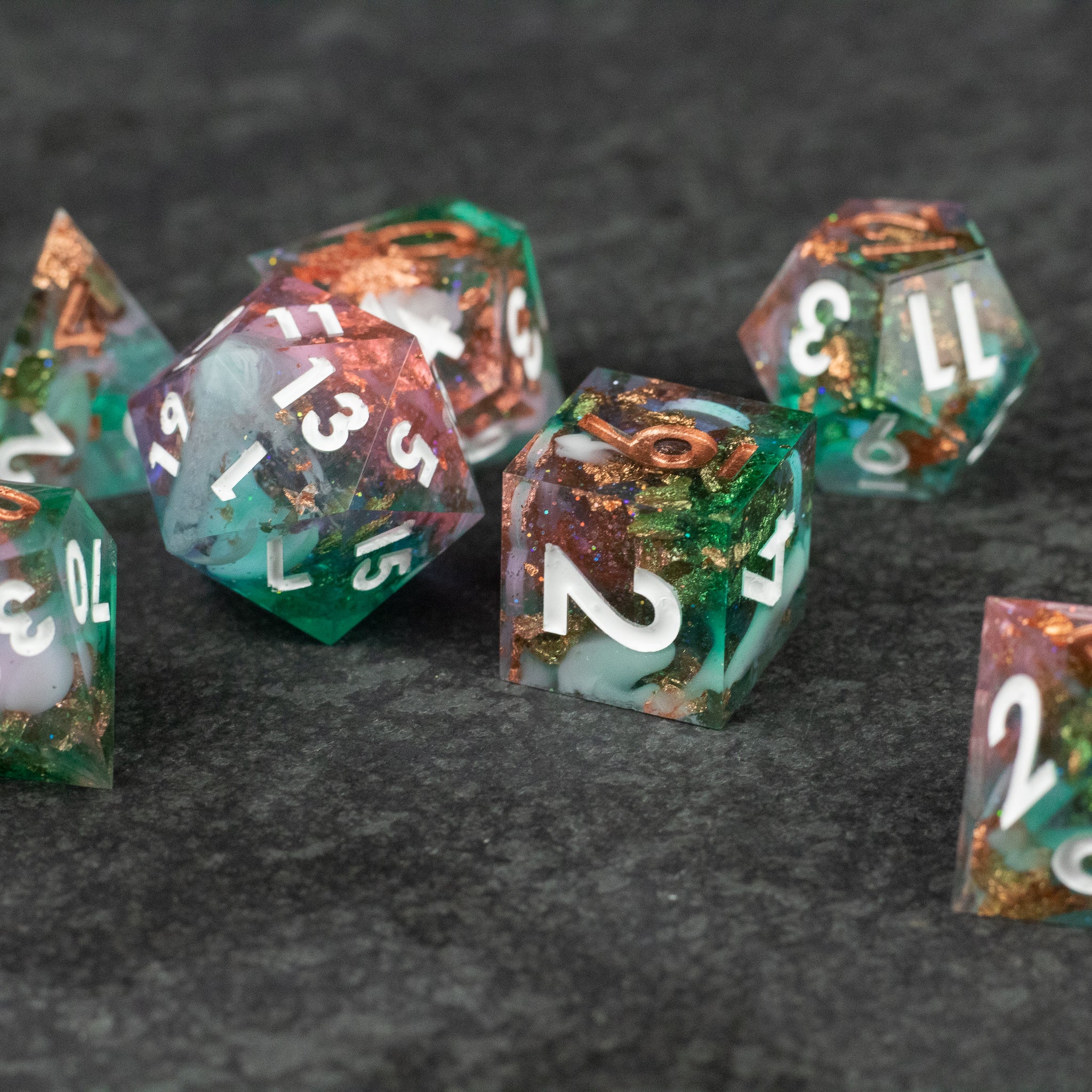 Scapeshift Dice Set - Translucent green and orange sharp-edged polyhedral dice set with white numbering on dark textured surface.