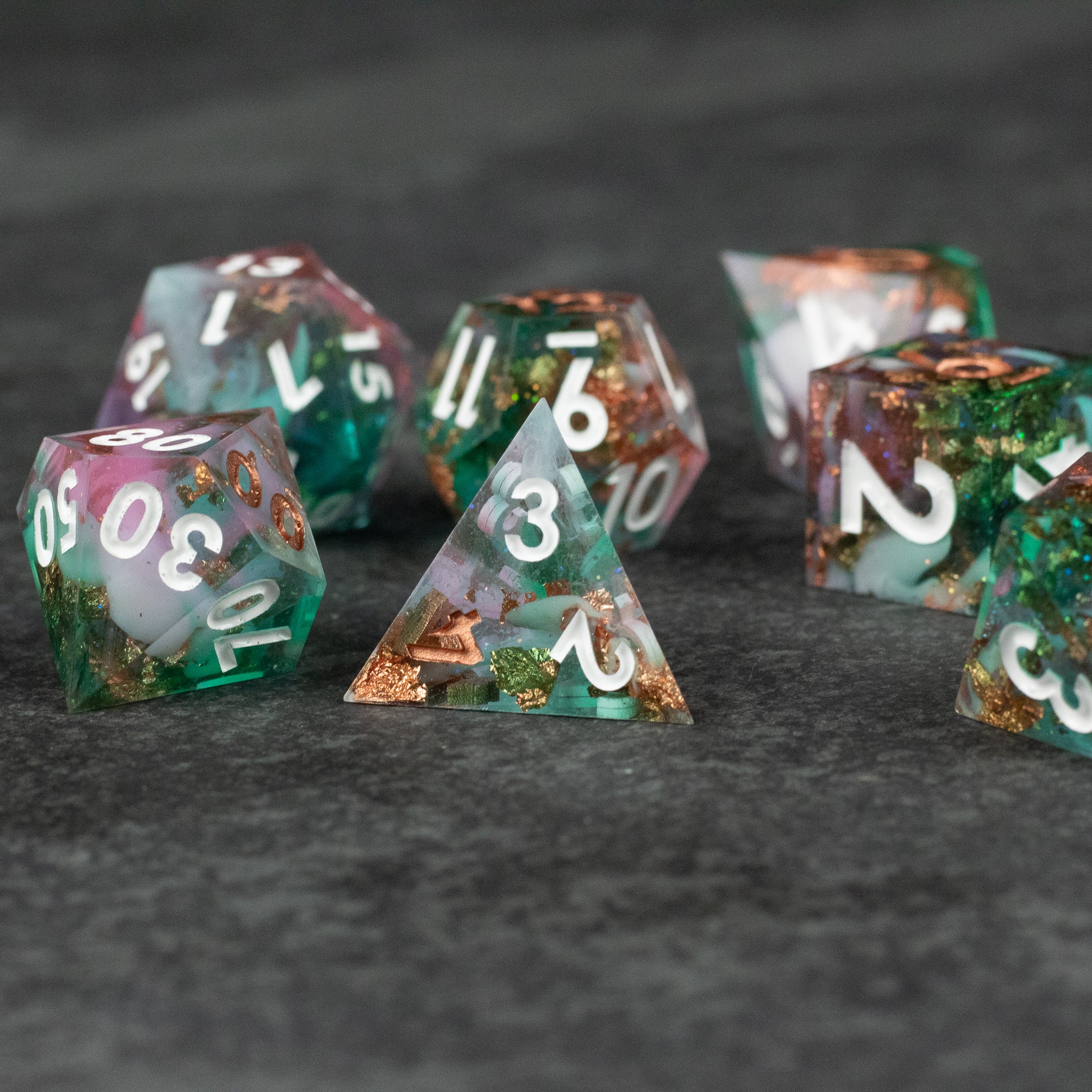 Scapeshift Dice Set - Seven polyhedral dice in green and copper swirls with sharp edges and white numbering on a dark textured surface.