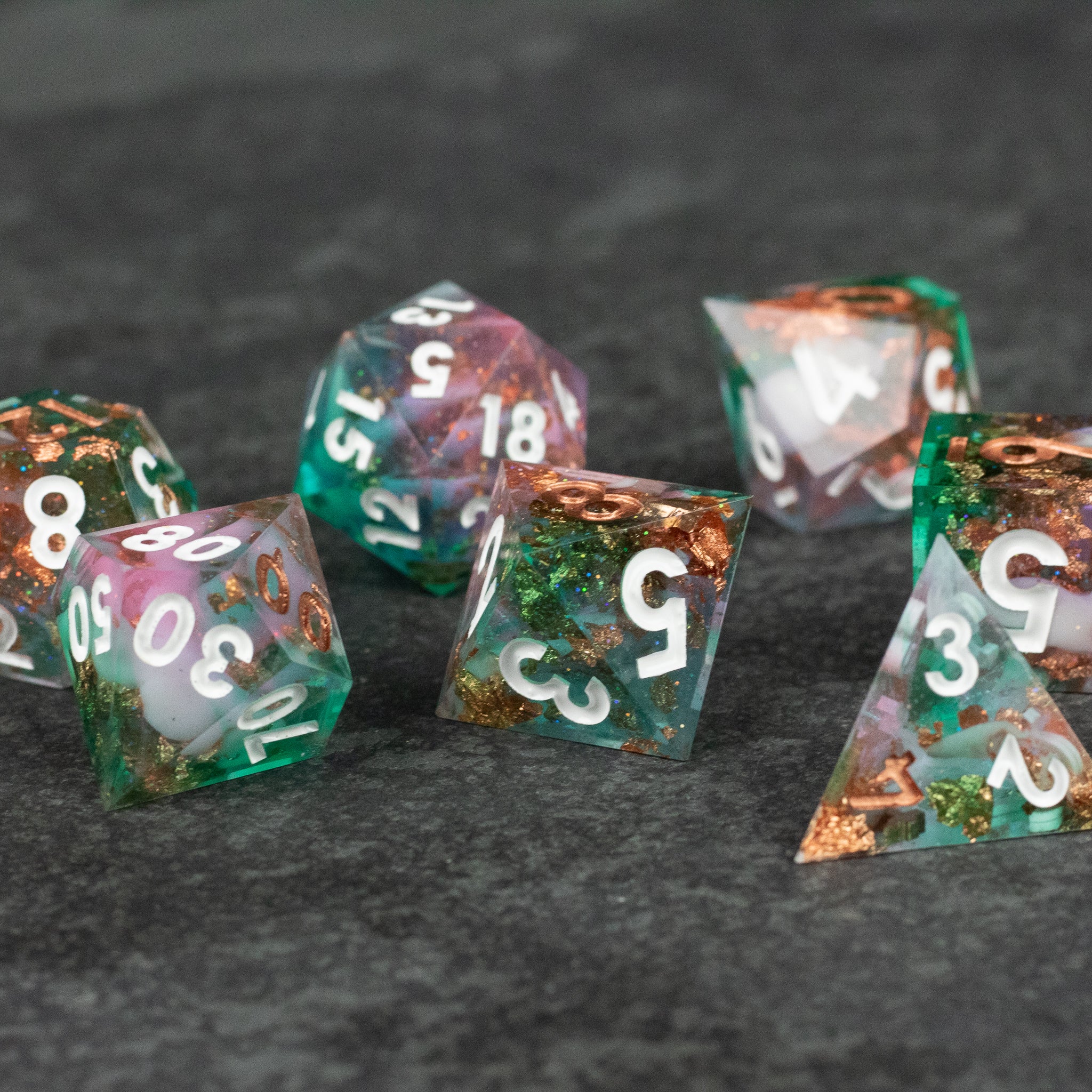 Scapeshift Dice Set - Translucent green and copper sharp-edged polyhedral dice set with white numbers on a dark textured surface.