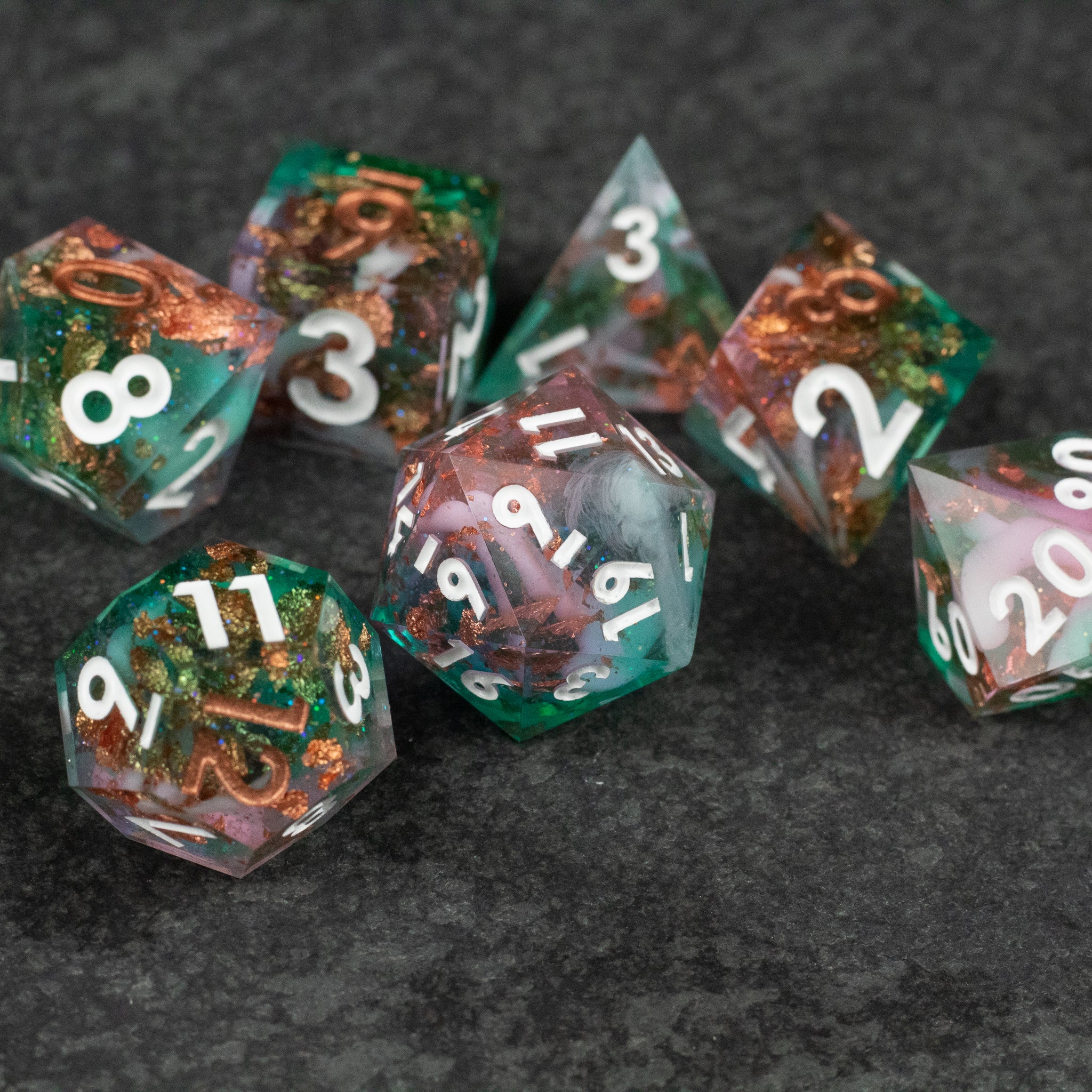 Scapeshift Dice Set - Seven-piece translucent polyhedral dice set with sharp edges, blending green and copper swirls, white numbers.