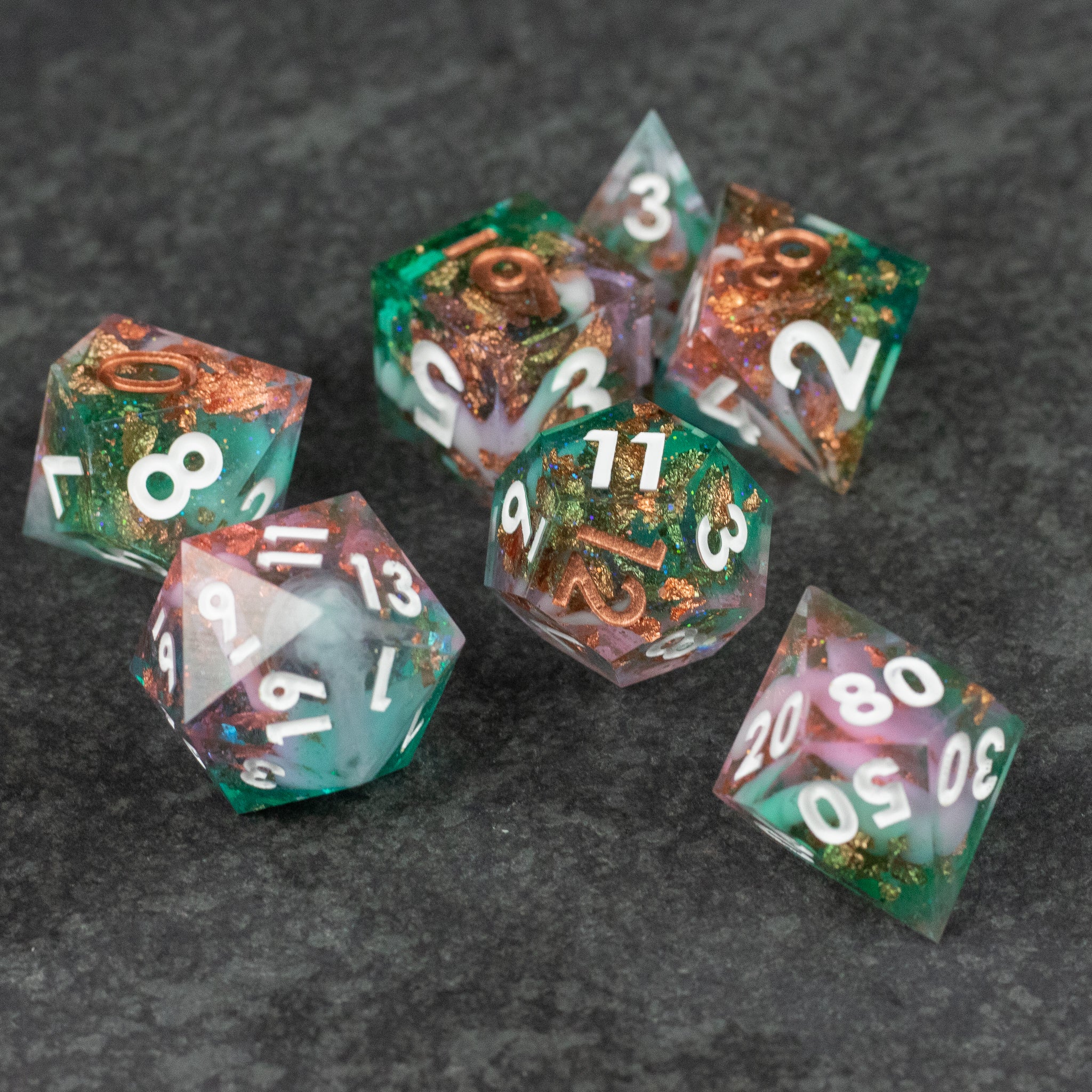 Scapeshift Dice Set - Seven sharp-edged polyhedral dice with green, copper, and white marbled translucent design on dark surface.