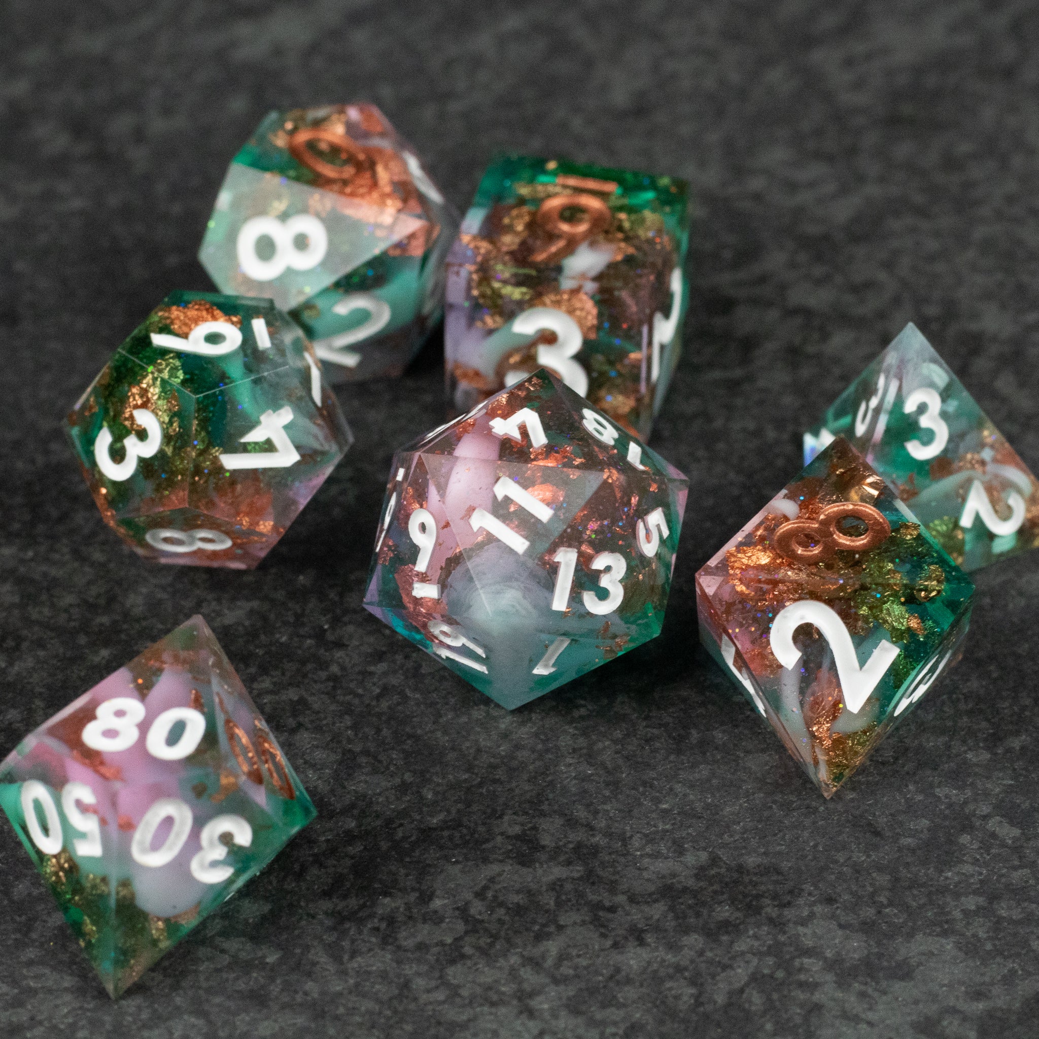 Scapeshift Dice Set - Set of seven translucent sharp-edged dice with green, pink, and copper metallic swirls and white numbers.