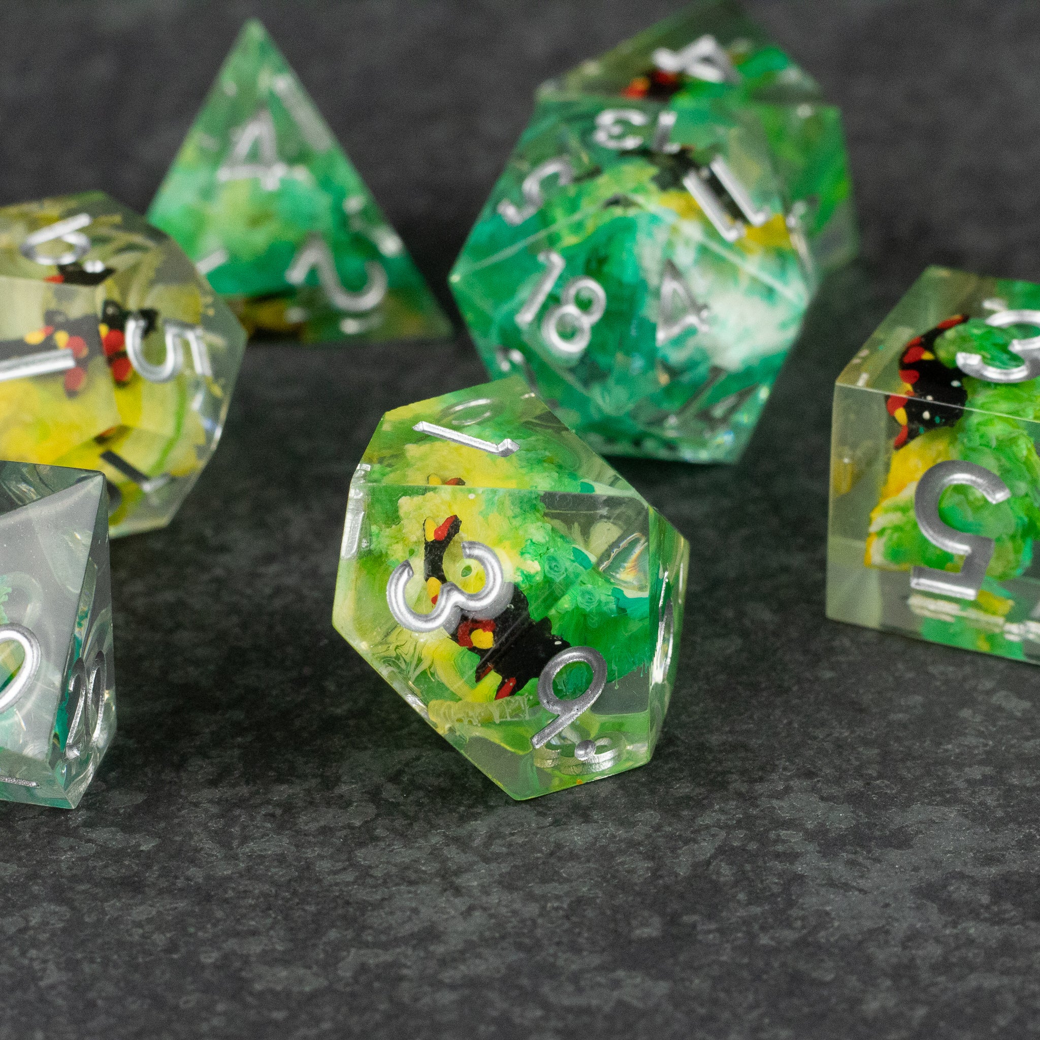 Green Lagoon Dice Set - Set of sharp-edged polyhedral dice with green, yellow, and black swirling inclusions and white numbering on a dark surface.