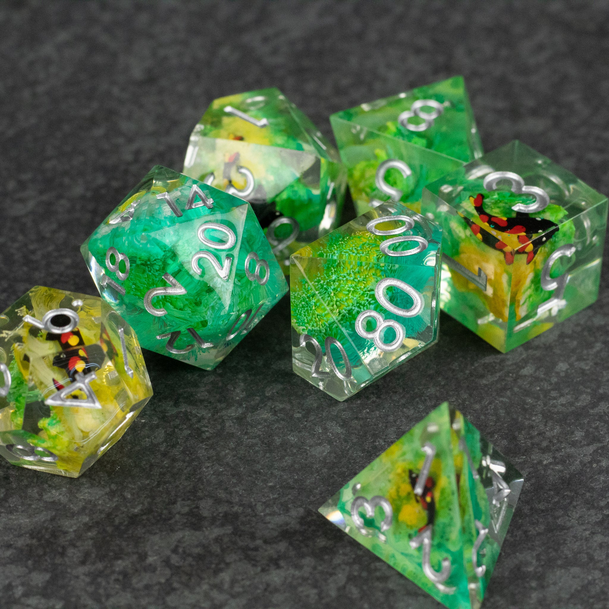 Green Lagoon Dice Set - Seven translucent green polyhedral dice with embedded colorful inclusions and white numbering on a dark surface.