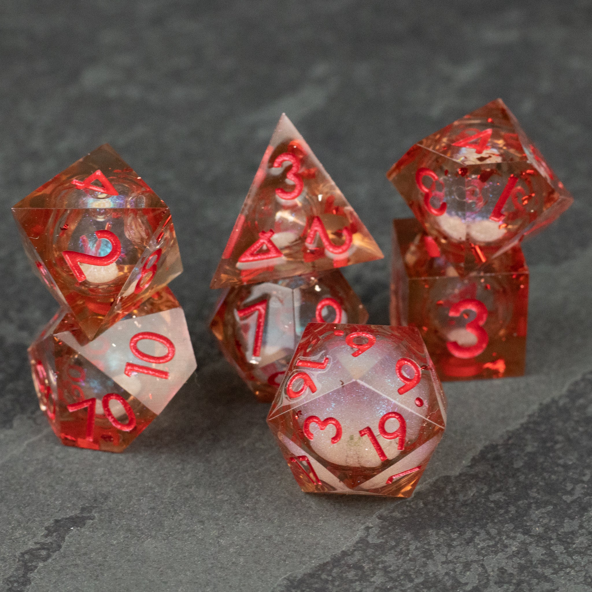 Potion of Fire Breath - Liquid Core Dice Set - Seven-piece sharp-edged translucent red liquid core dice set with gold numbering on dark stone background.