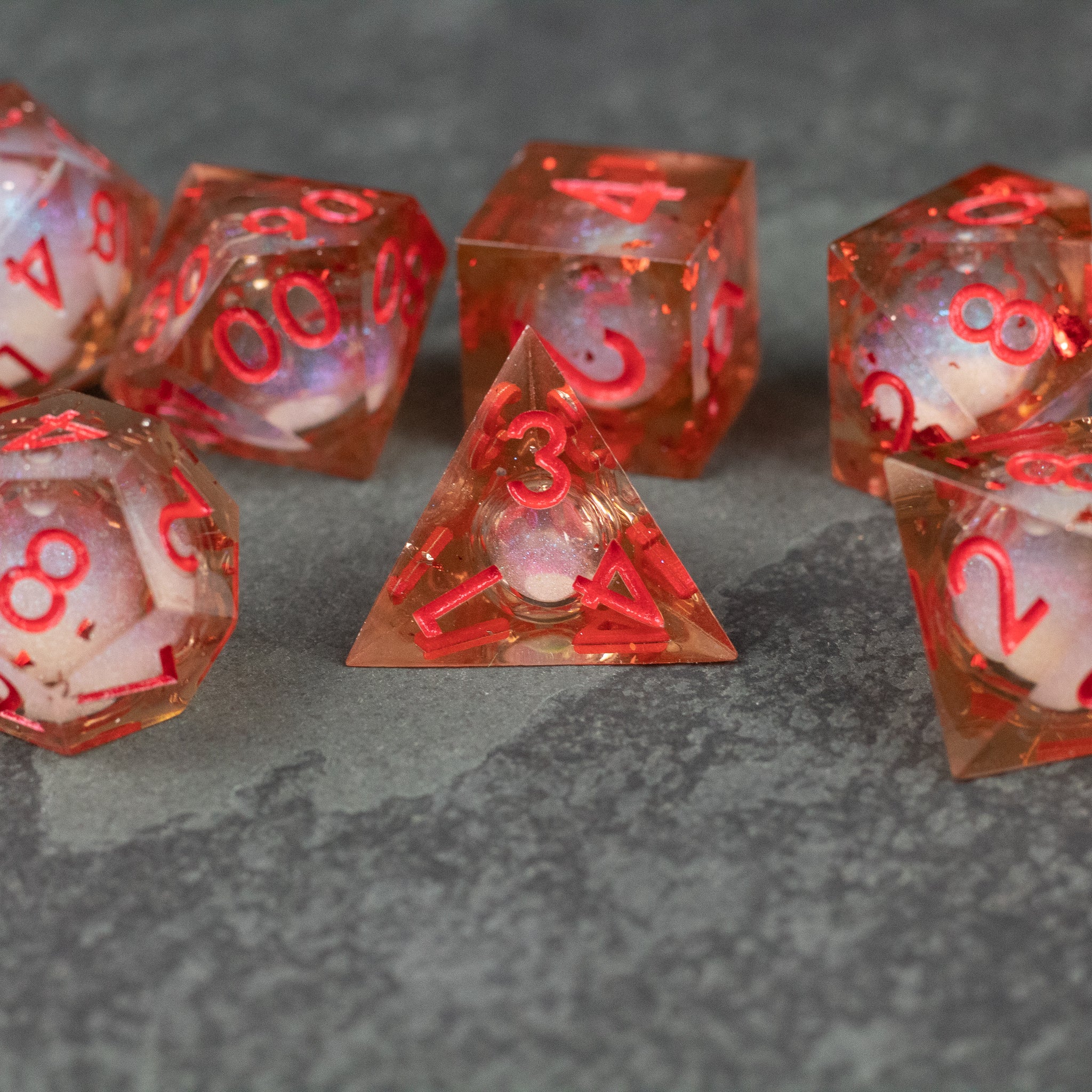 Potion of Fire Breath - Liquid Core Dice Set - Translucent orange liquid core dice set with sharp edges and red numbers on a gray surface.