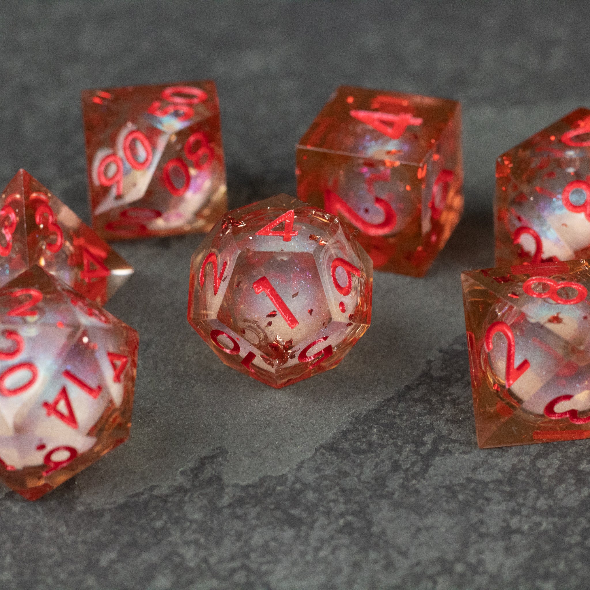 Potion of Fire Breath - Liquid Core Dice Set - Transparent dice set with red liquid core and red sharp-edged numbers on gray surface.