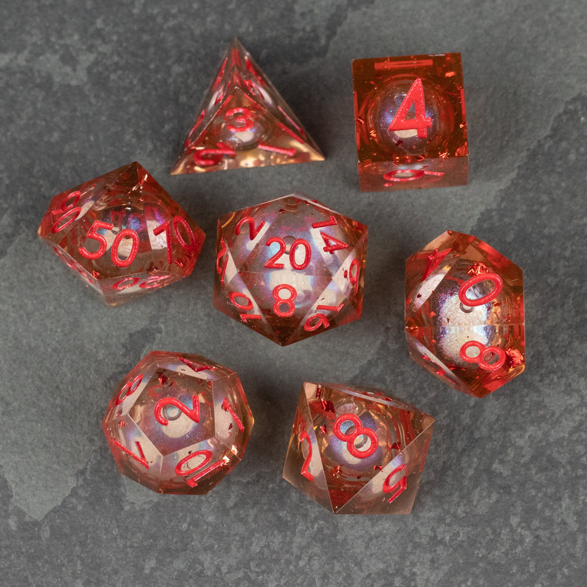 Potion of Fire Breath - Liquid Core Dice Set - Seven red translucent polyhedral dice with liquid core and sharp edges on gray surface.