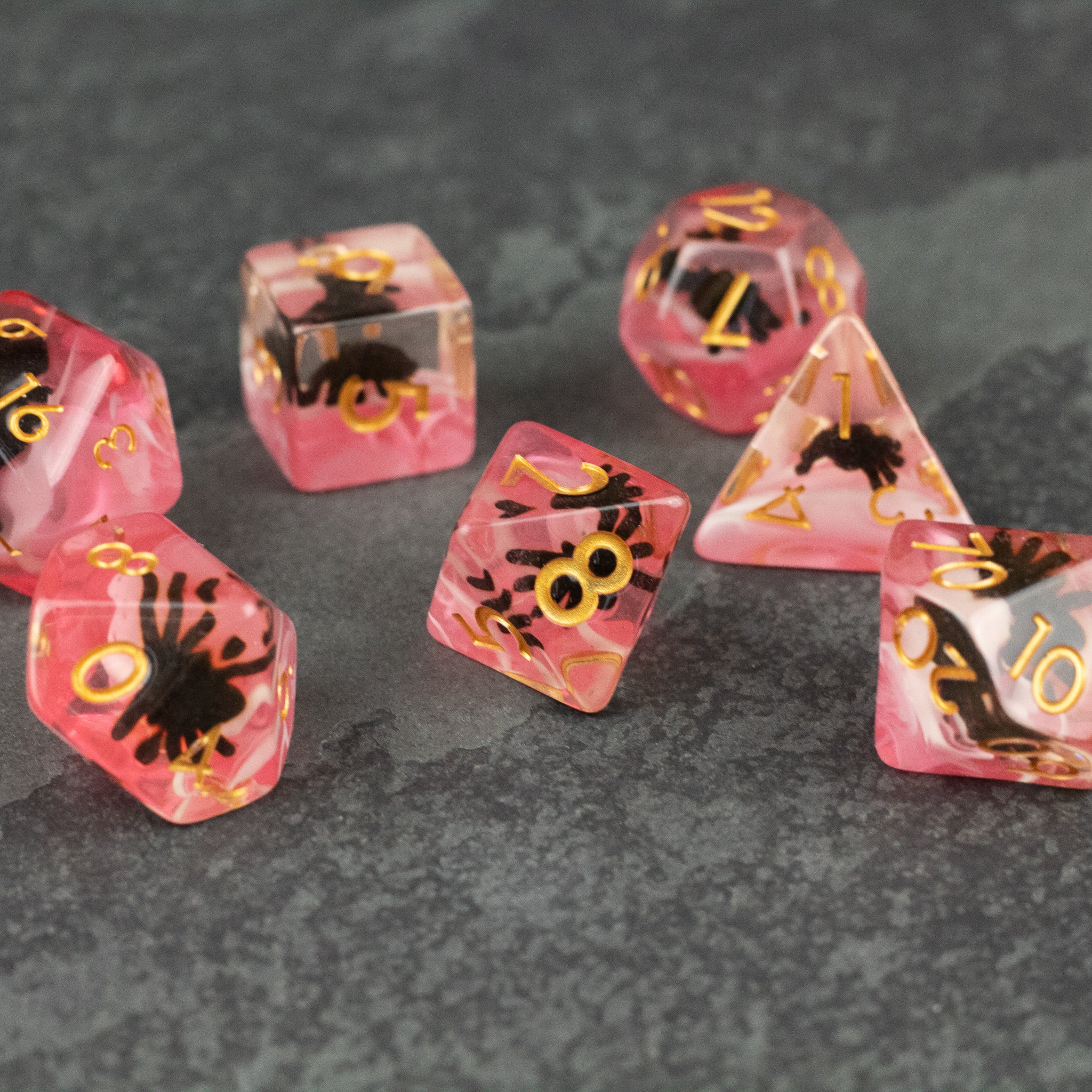 Black Spider Dice Set - Red - Translucent red polyhedral dice set with gold numbers and black spider silhouettes inside.