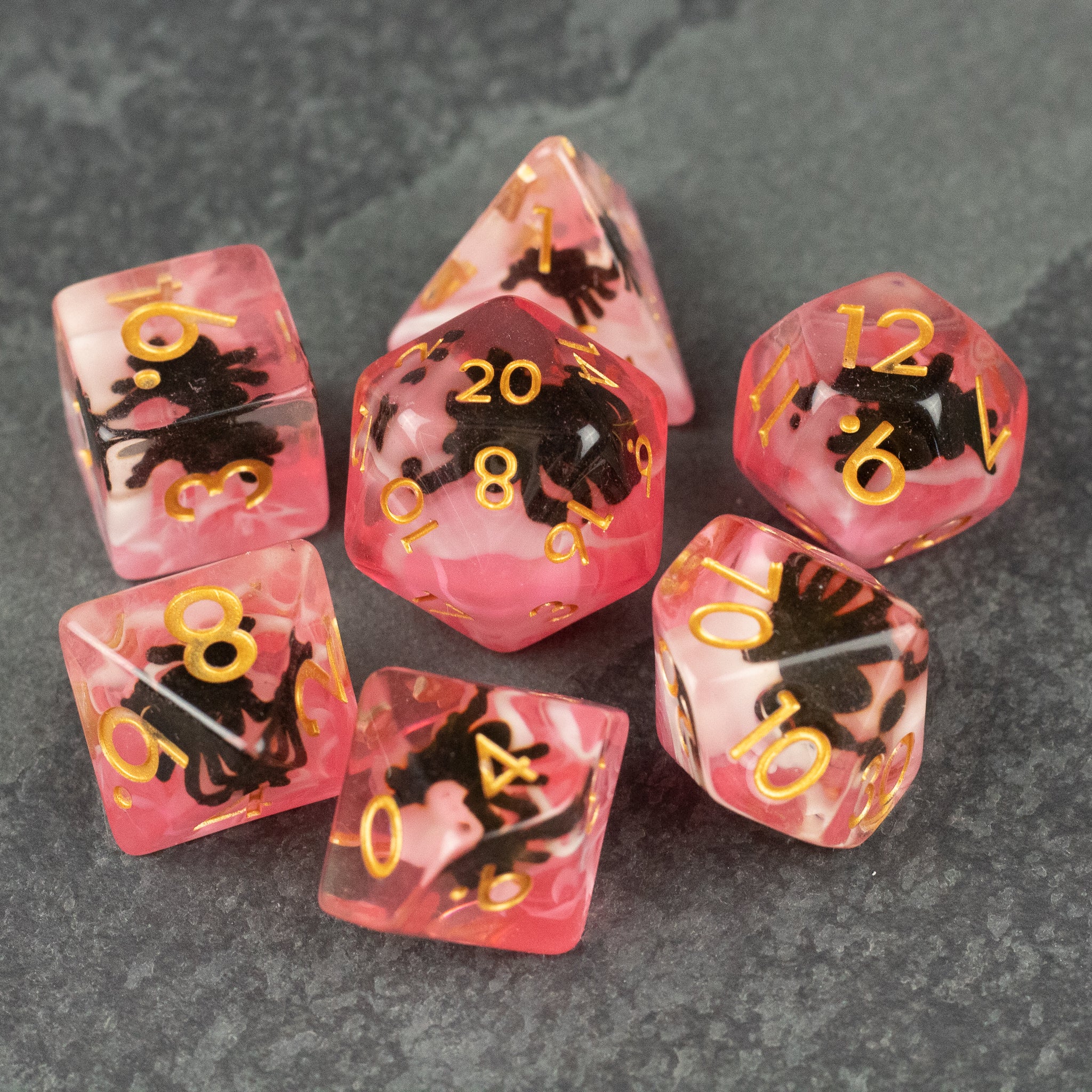 Black Spider Dice Set - Red - Set of seven red translucent polyhedral dice with black spider designs and gold numbers on a gray stone surface.