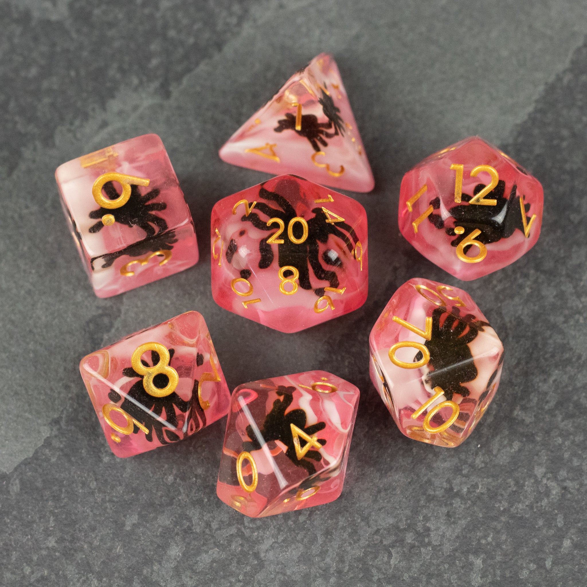 Black Spider Dice Set - Red - Seven red translucent dice with black spider silhouettes and gold numbers on a dark gray surface.