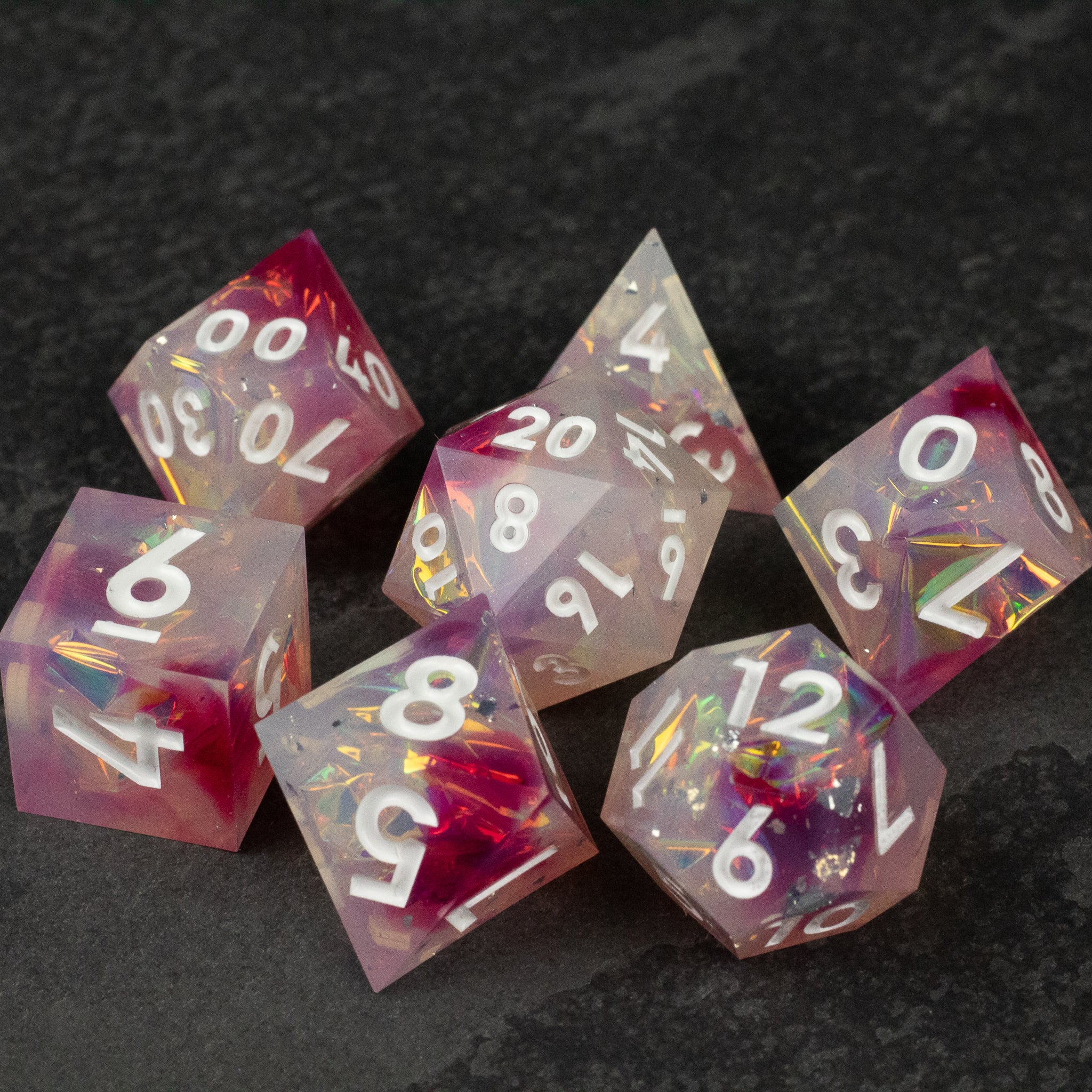 Lover's Kiss Dice Set - Set of seven translucent red and pink sharp-edged polyhedral dice with white numbering and embedded glitter flakes.
